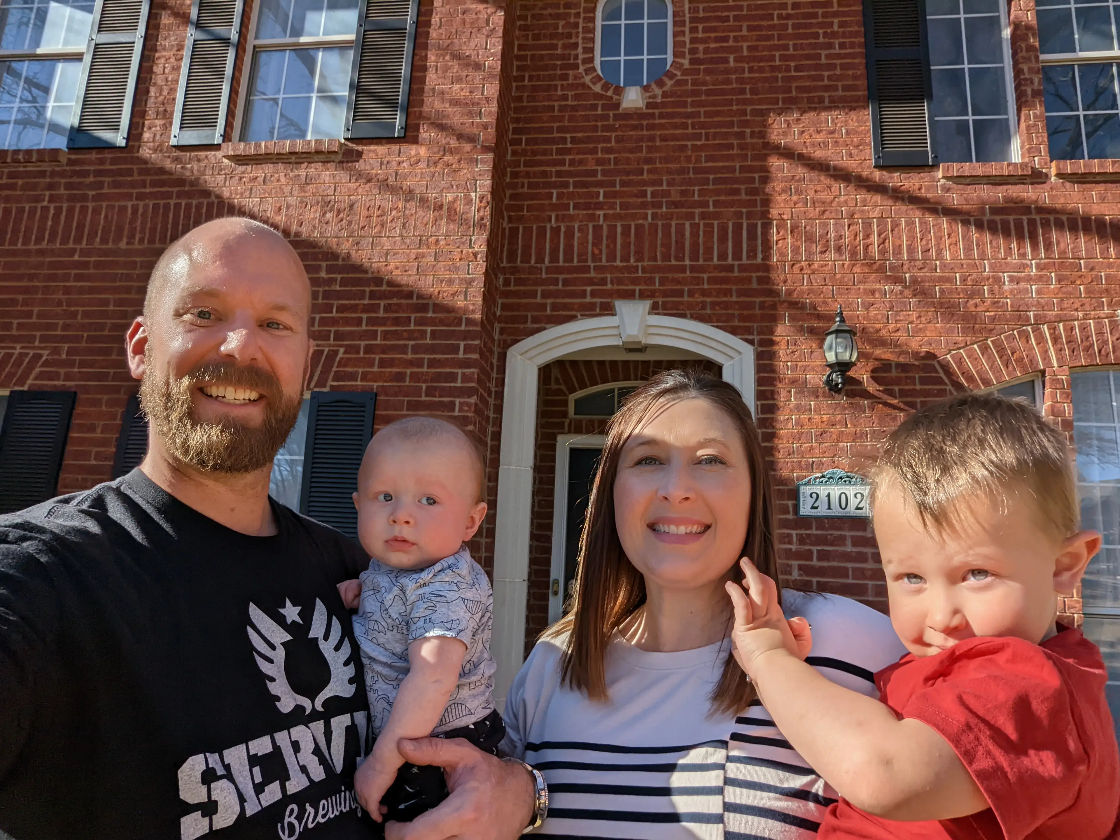 Family of four smiling in front of brick building