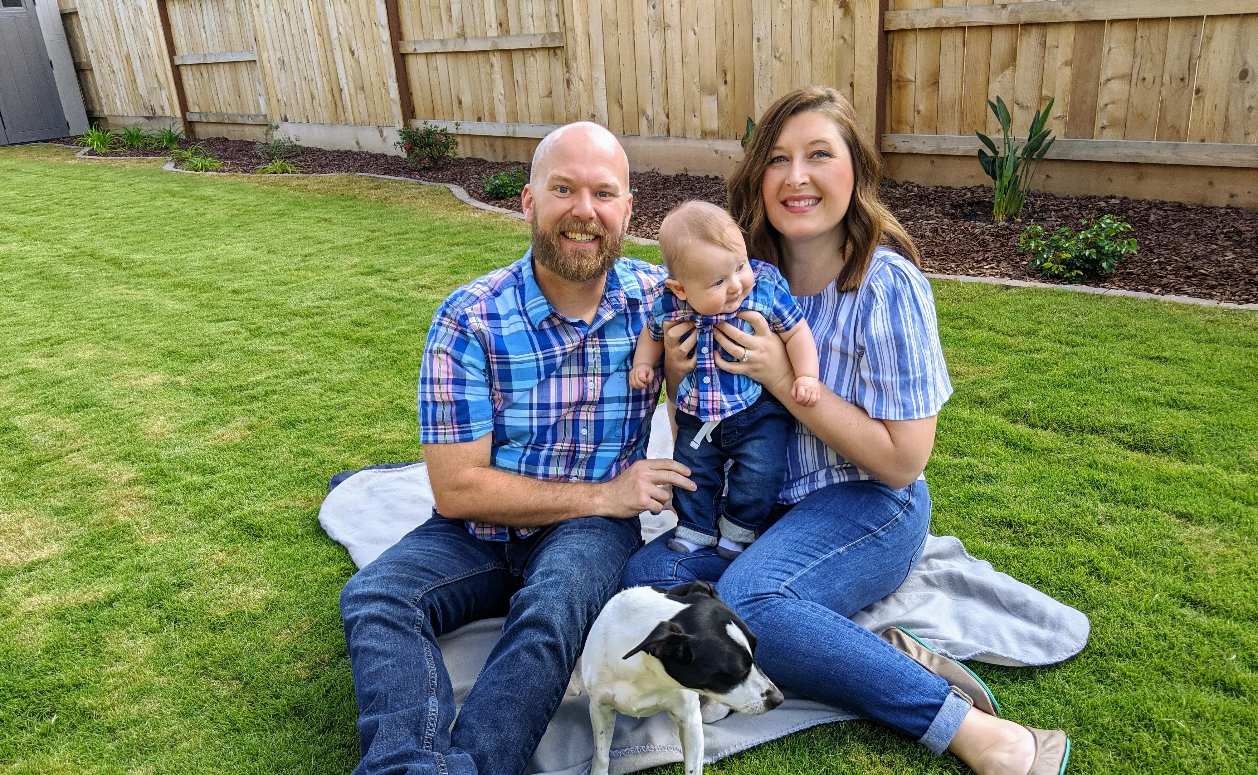 Couple smiling with baby wearinf plaid shirts in yard