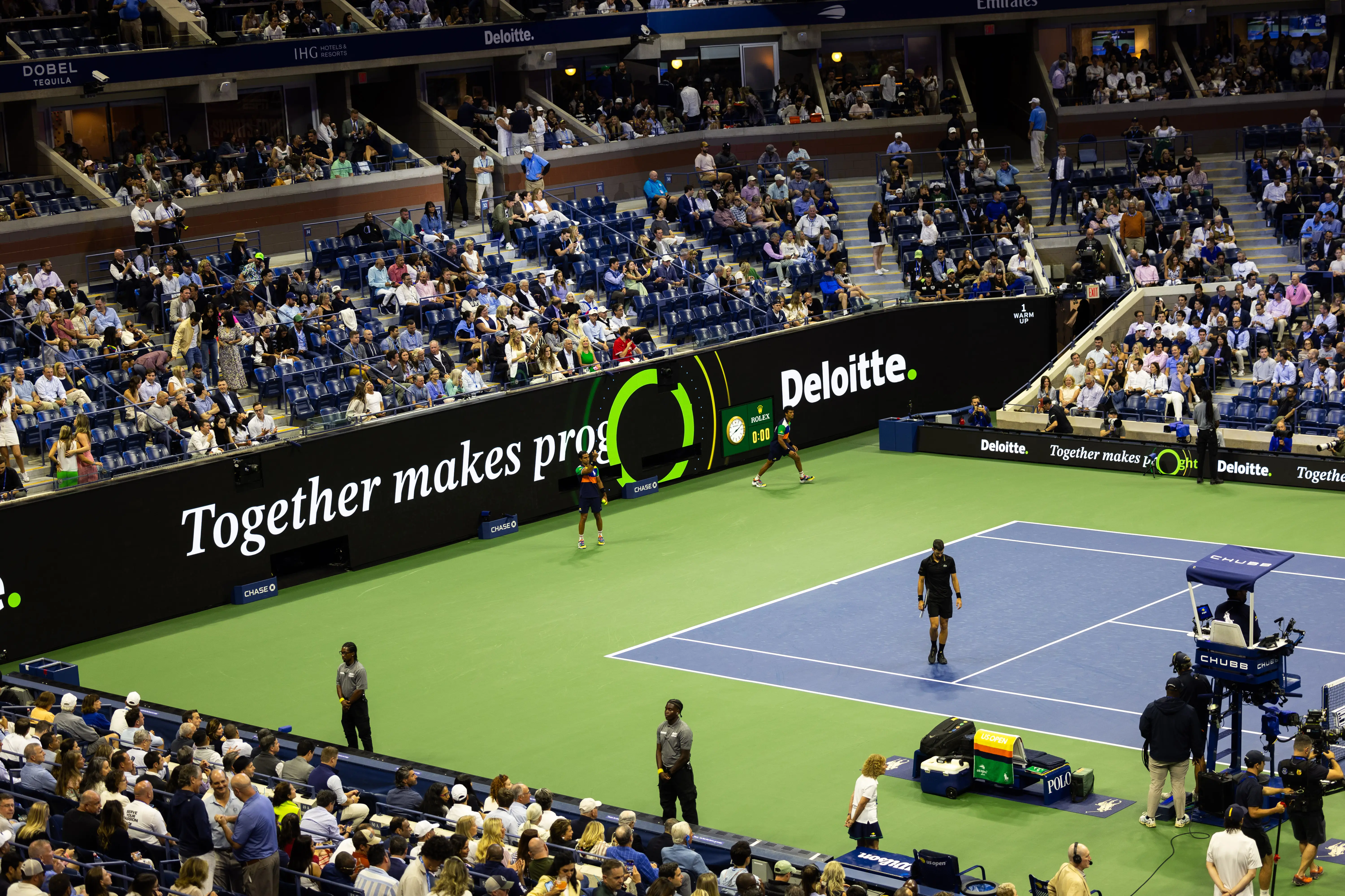 Image of a tennis match with a prominent sponsor logo, Deloitte