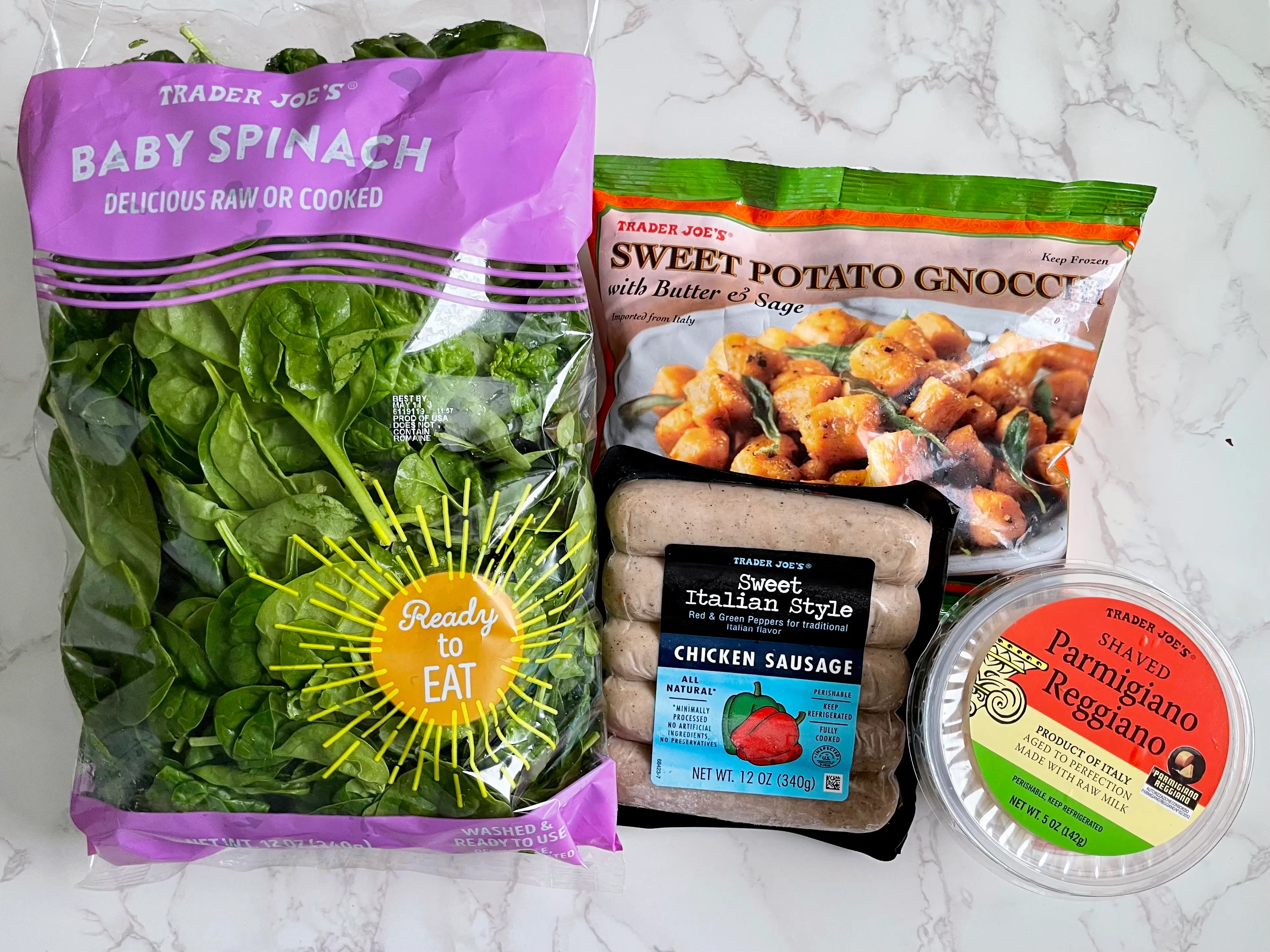 A bag of baby spinach, a bag of sweet potato gnocchi, a package of chicken sausage, and a container of shaved Parmigiano-Reggiano — all from Trader Joe's — on a countertop.
