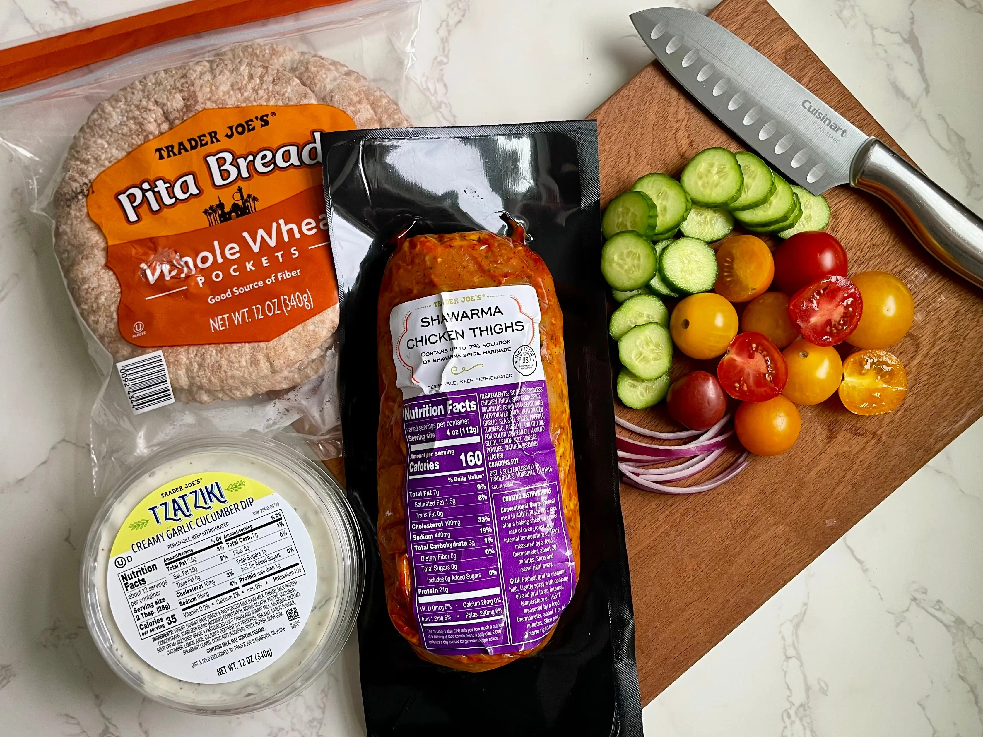 A package of pita bread, a container of tzatziki dip, a package of shawarma chicken thighs, and chopped cucumber, tomato, and onion — all from Trader Joe's — on a countertop.