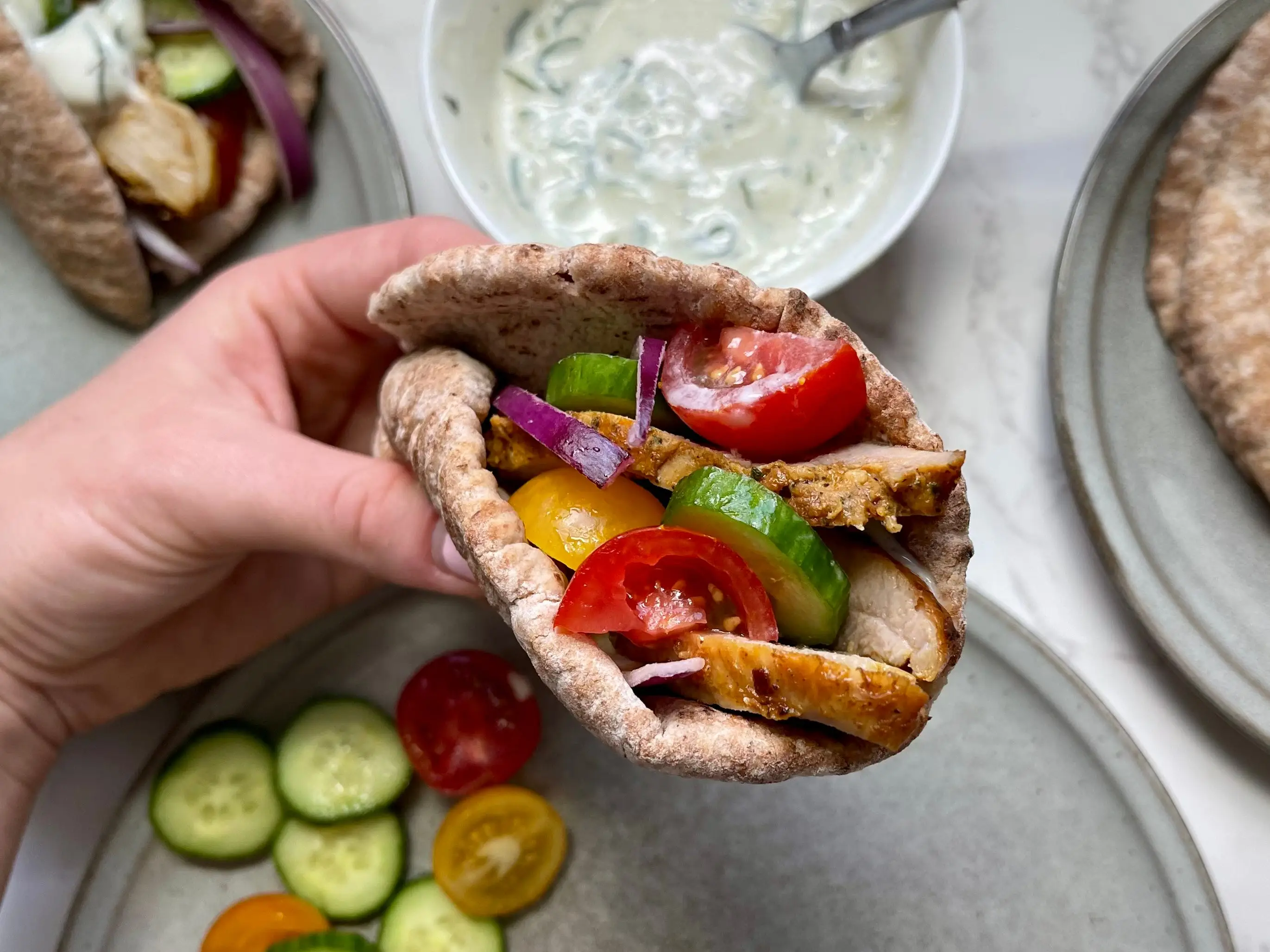 Serena holds a pita bread wrap with chicken, cucumbers, and onion, over the ingredients she used to make the meal.