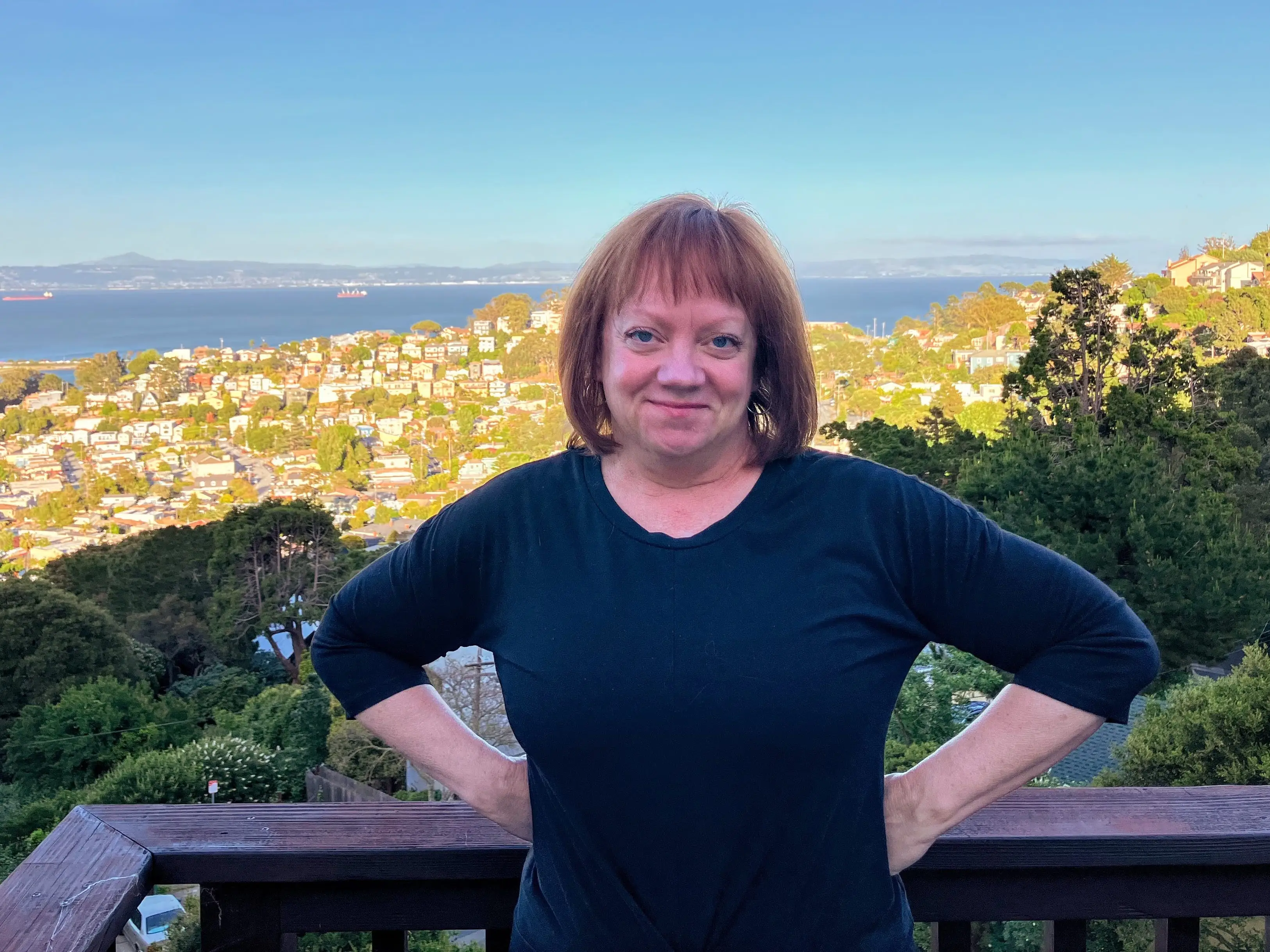 Woman with hands above hips smiling in front of aerial view of water, town