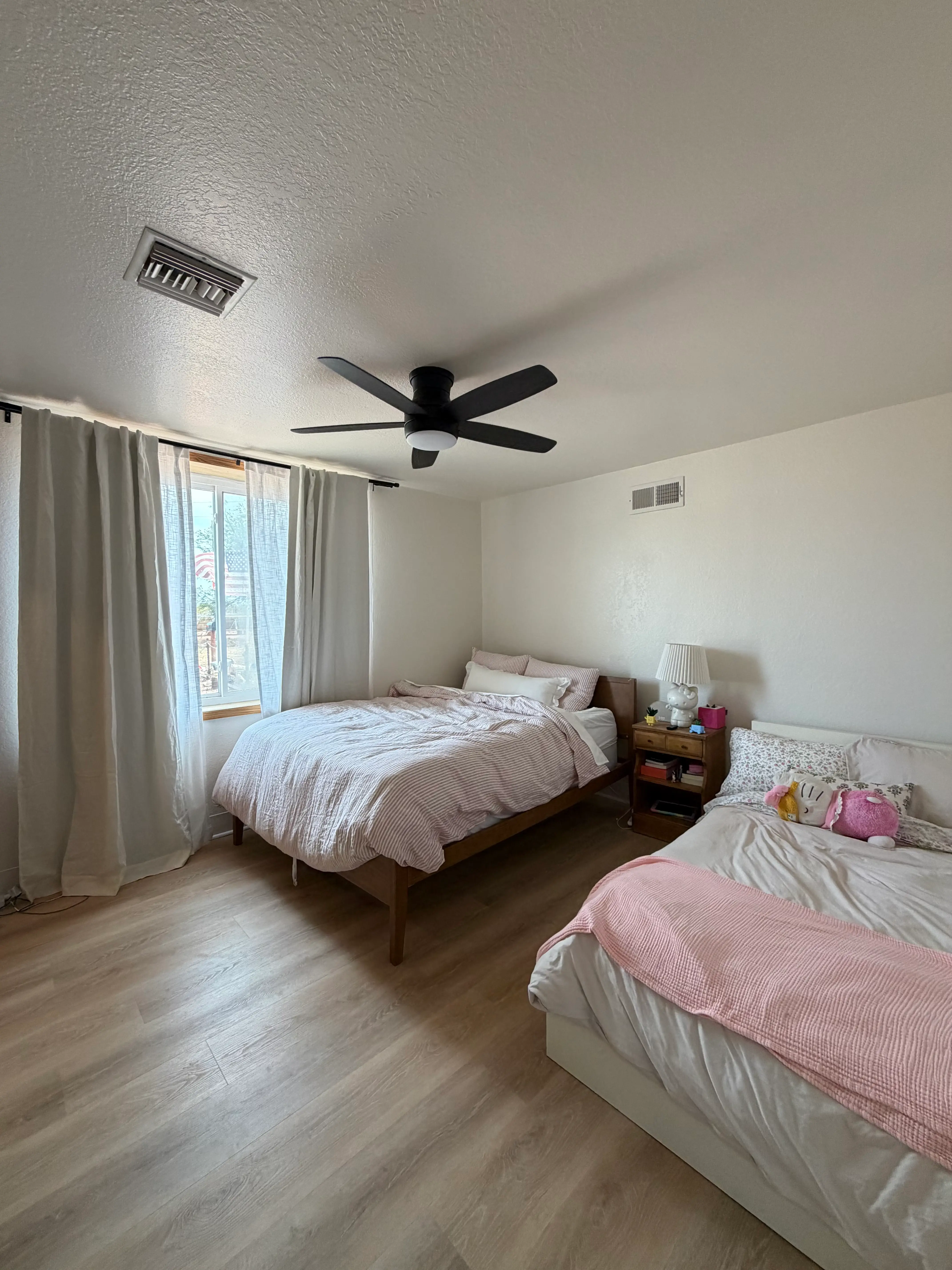 A bedroom with two beds, a window iwht curtains, and a nightstand.