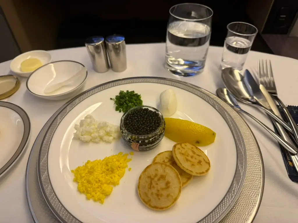 Plate of food next to water glass, silverware, salt and pepper shakers on white-cloth-covered table on plane