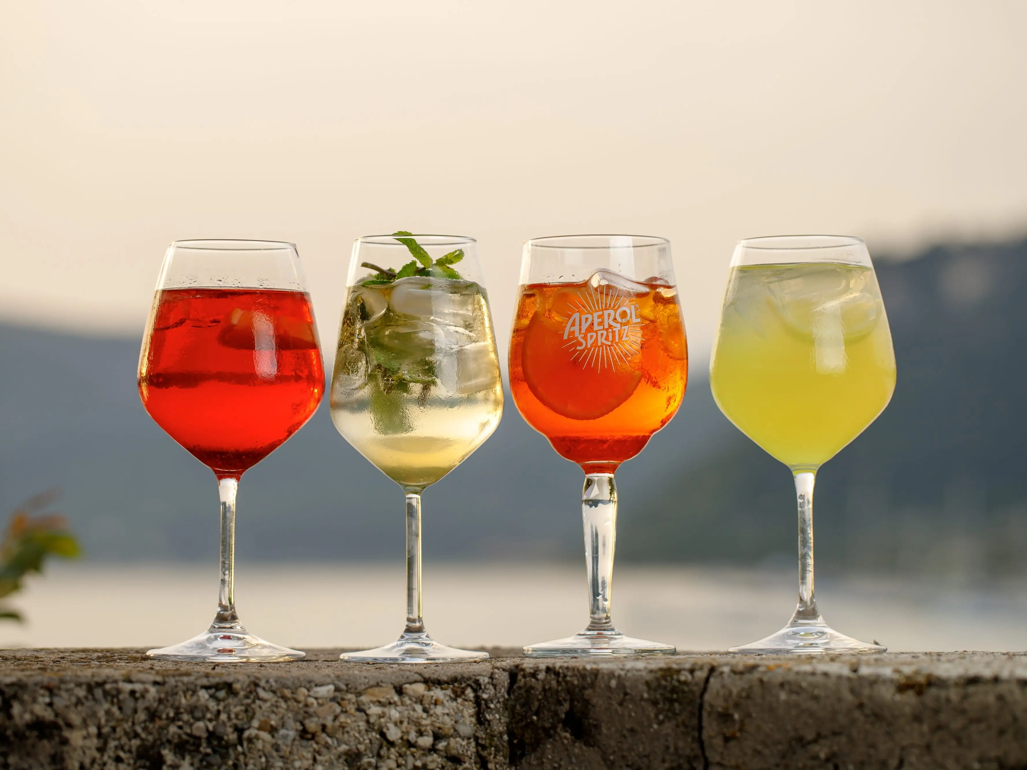 Four different alcoholic spritz drinks on a ledge.