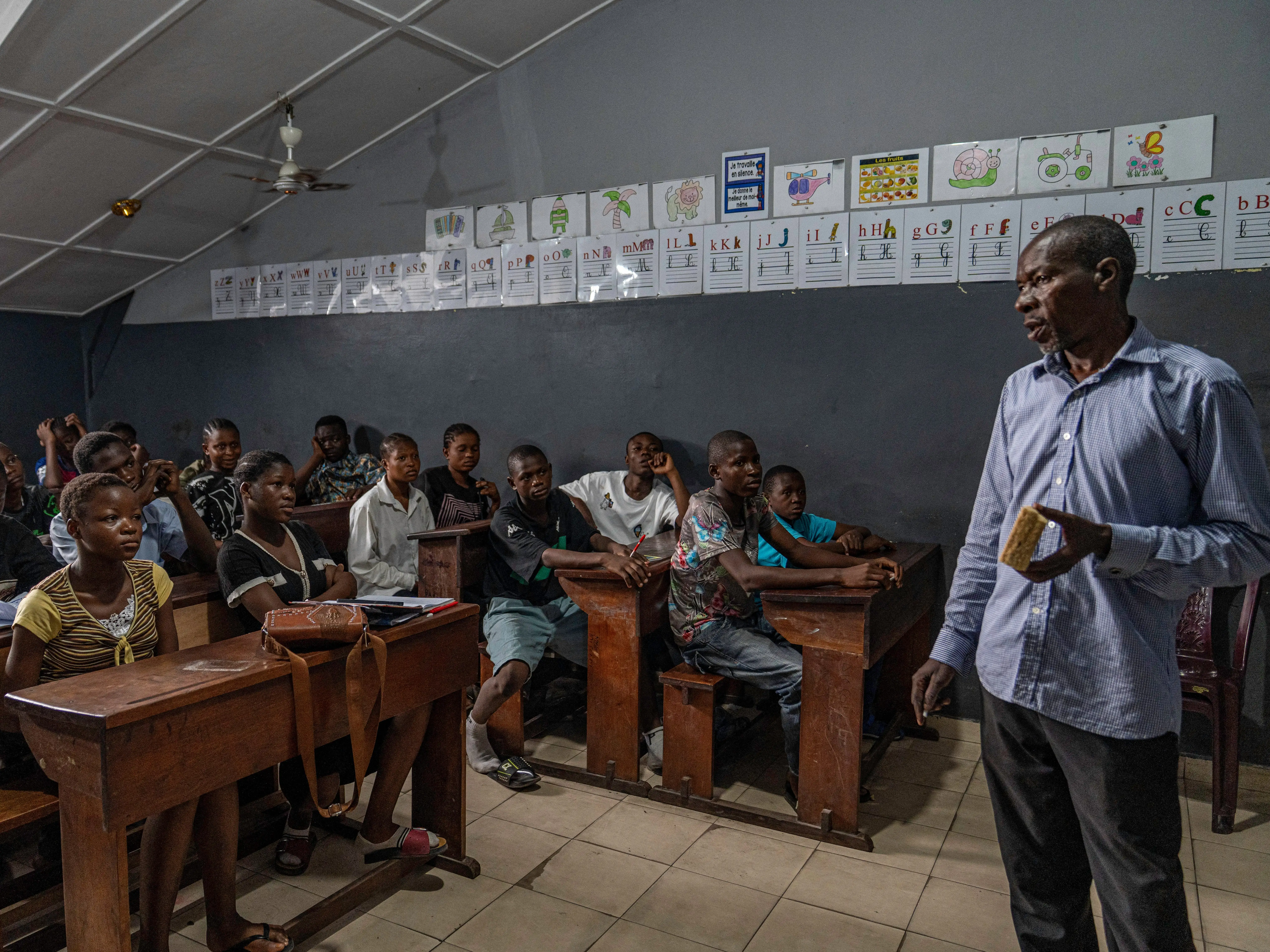 A teacher instructing a group of children sitting in desks.