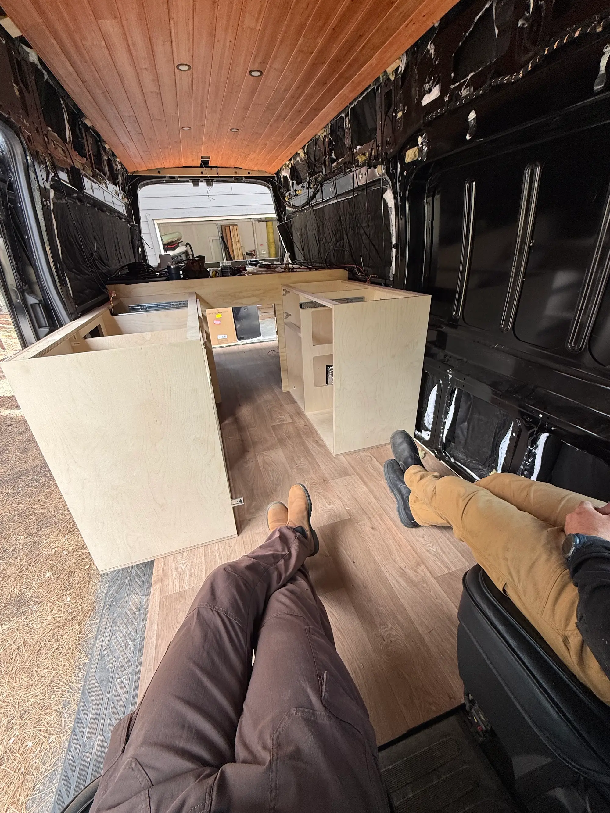 A van under construction with two pairs of legs visible in the bottom of the frame.