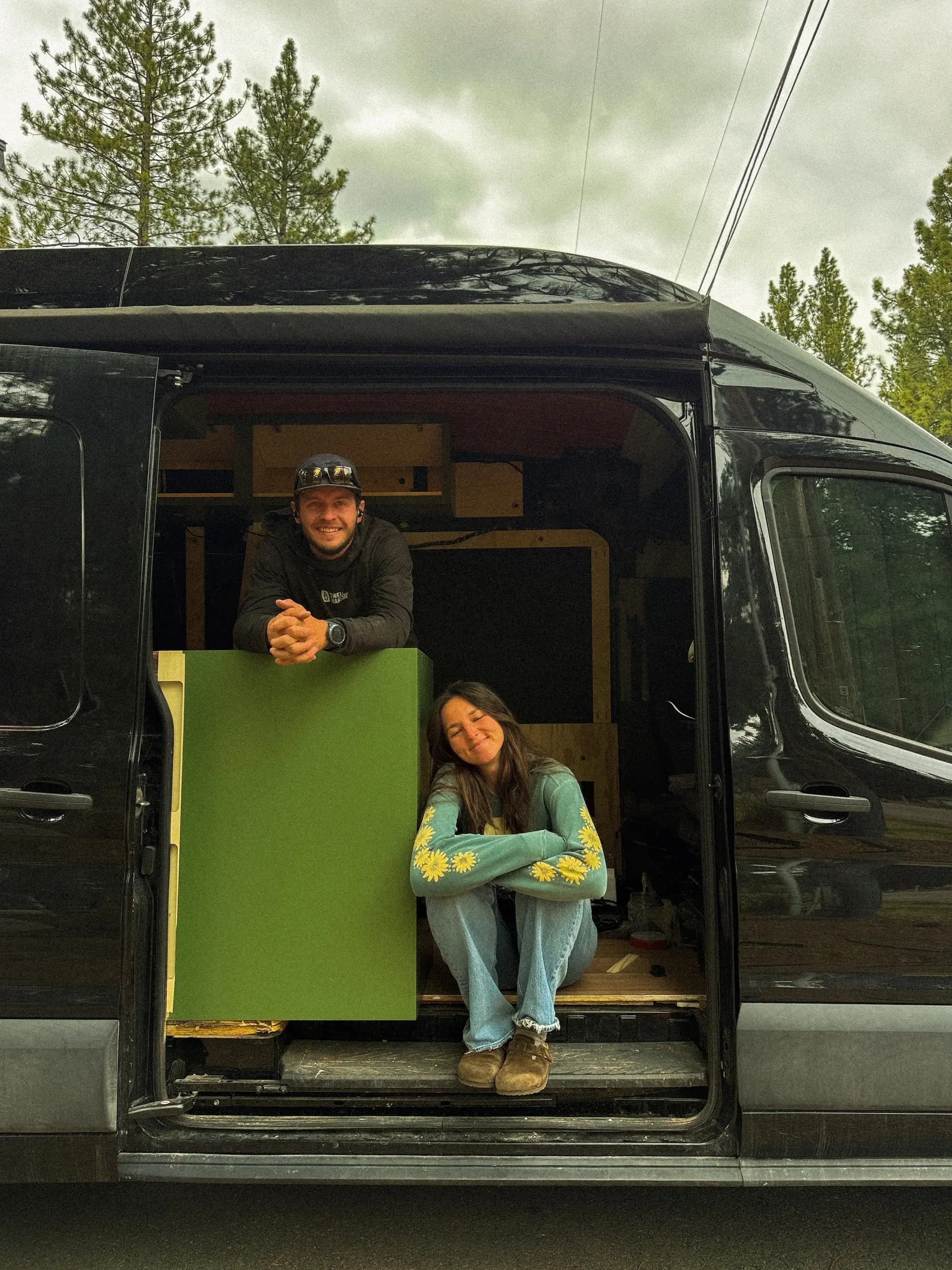 A couple smiles inside a van that is under construction.
