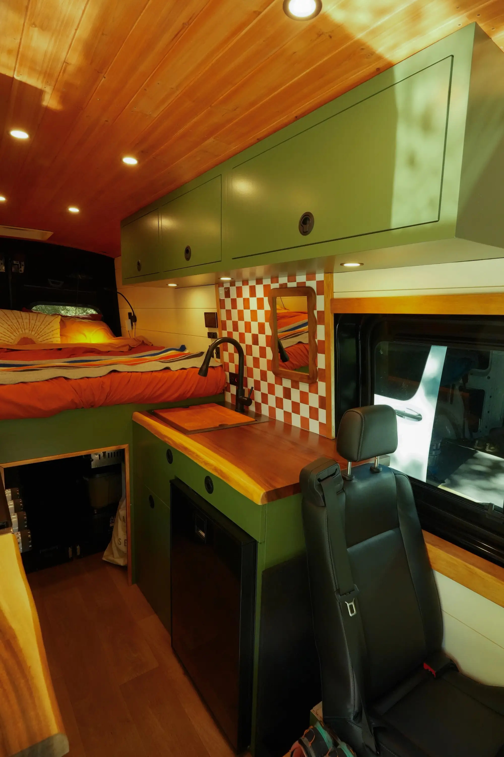 A van with green cabinetry, orange and white backsplash, wooden countertops, and a bed.