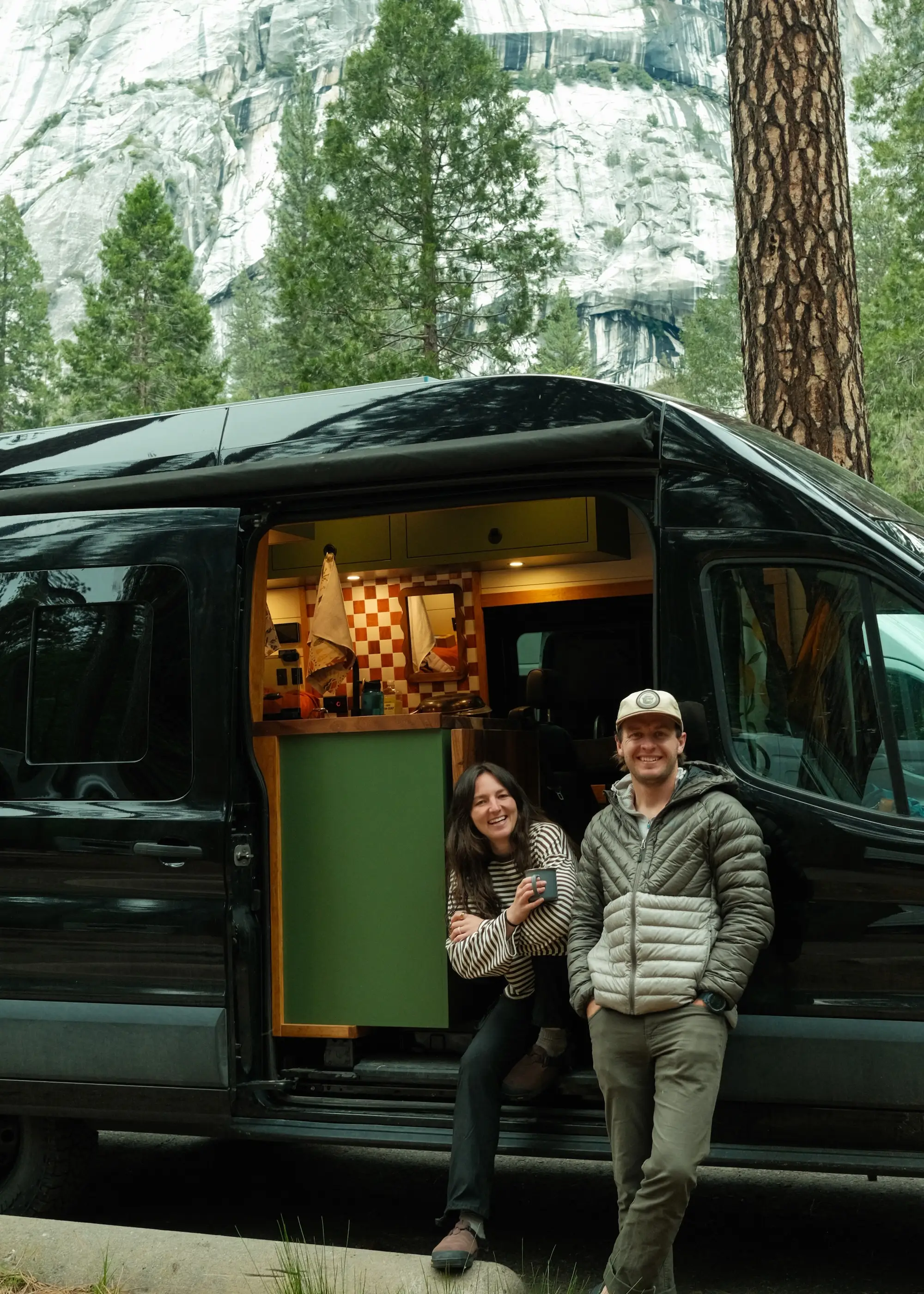 A couple sits on the open doorway of a black van.