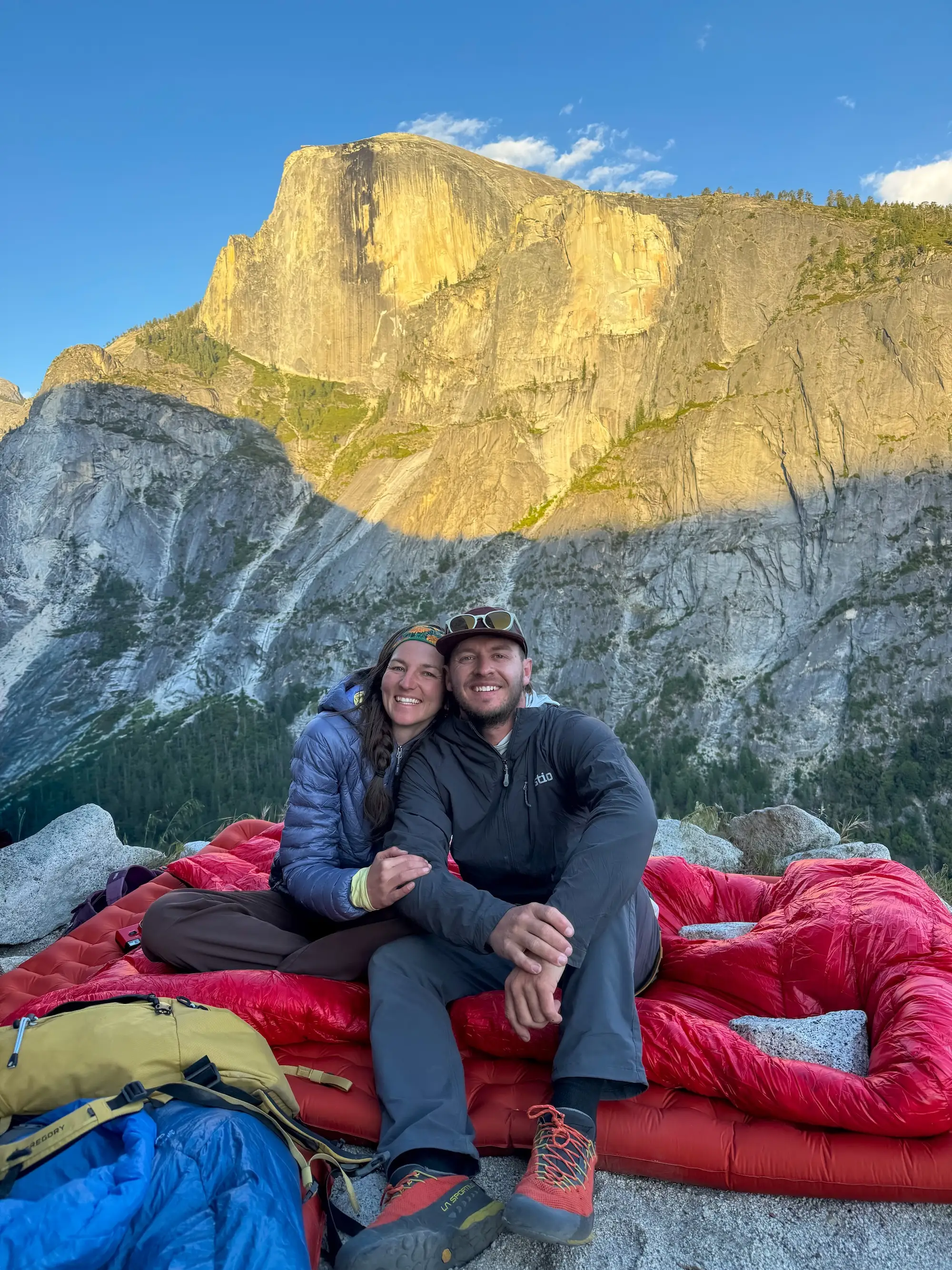 A couple leans together and smiles in front of a mountain.