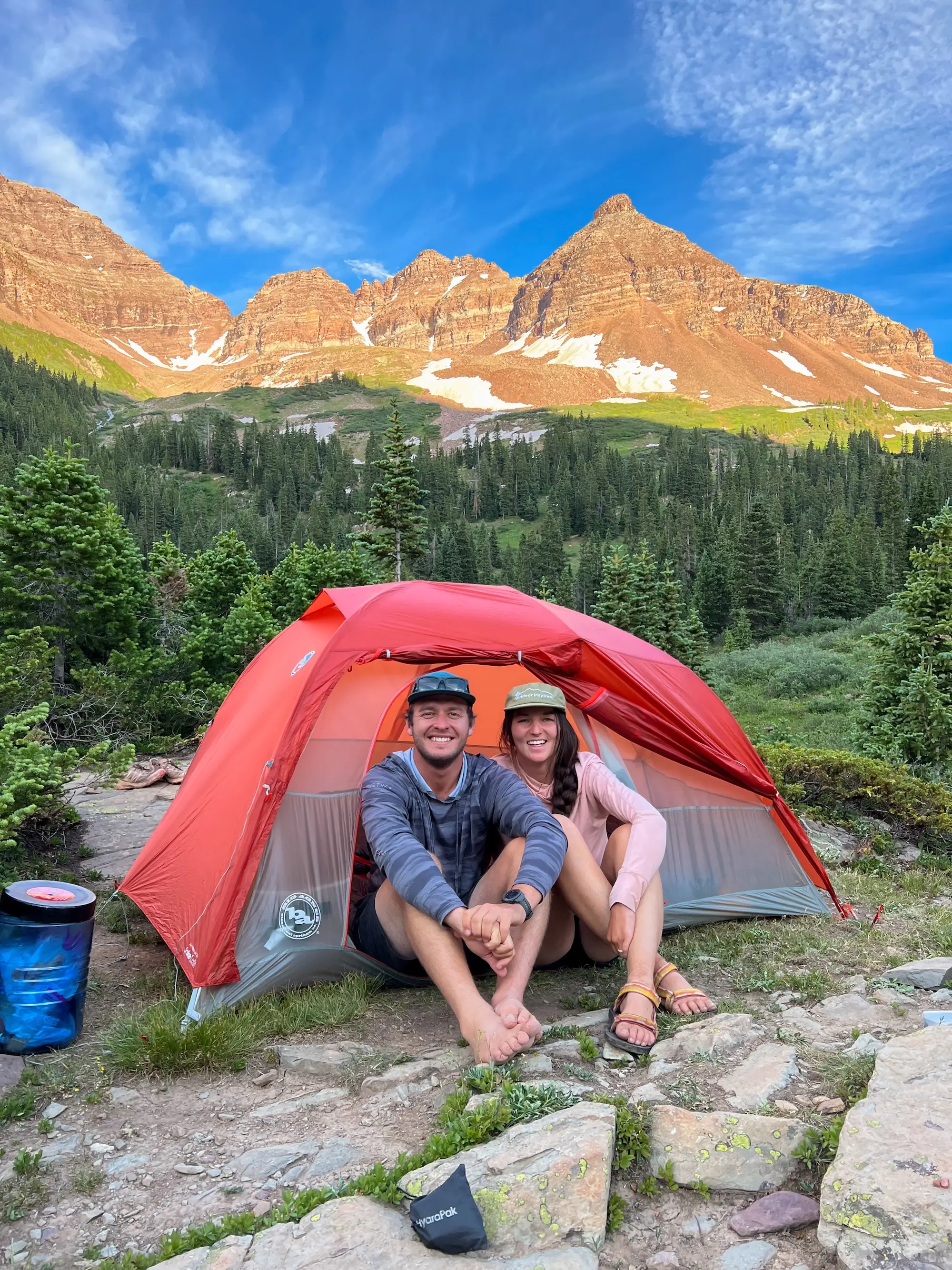A couple smiles from the entrance of a tent with mountains behind them.
