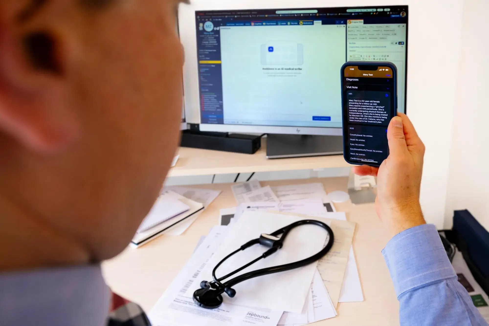 A man uses an AI scribe device on his iPhone with a computer behind the phone.