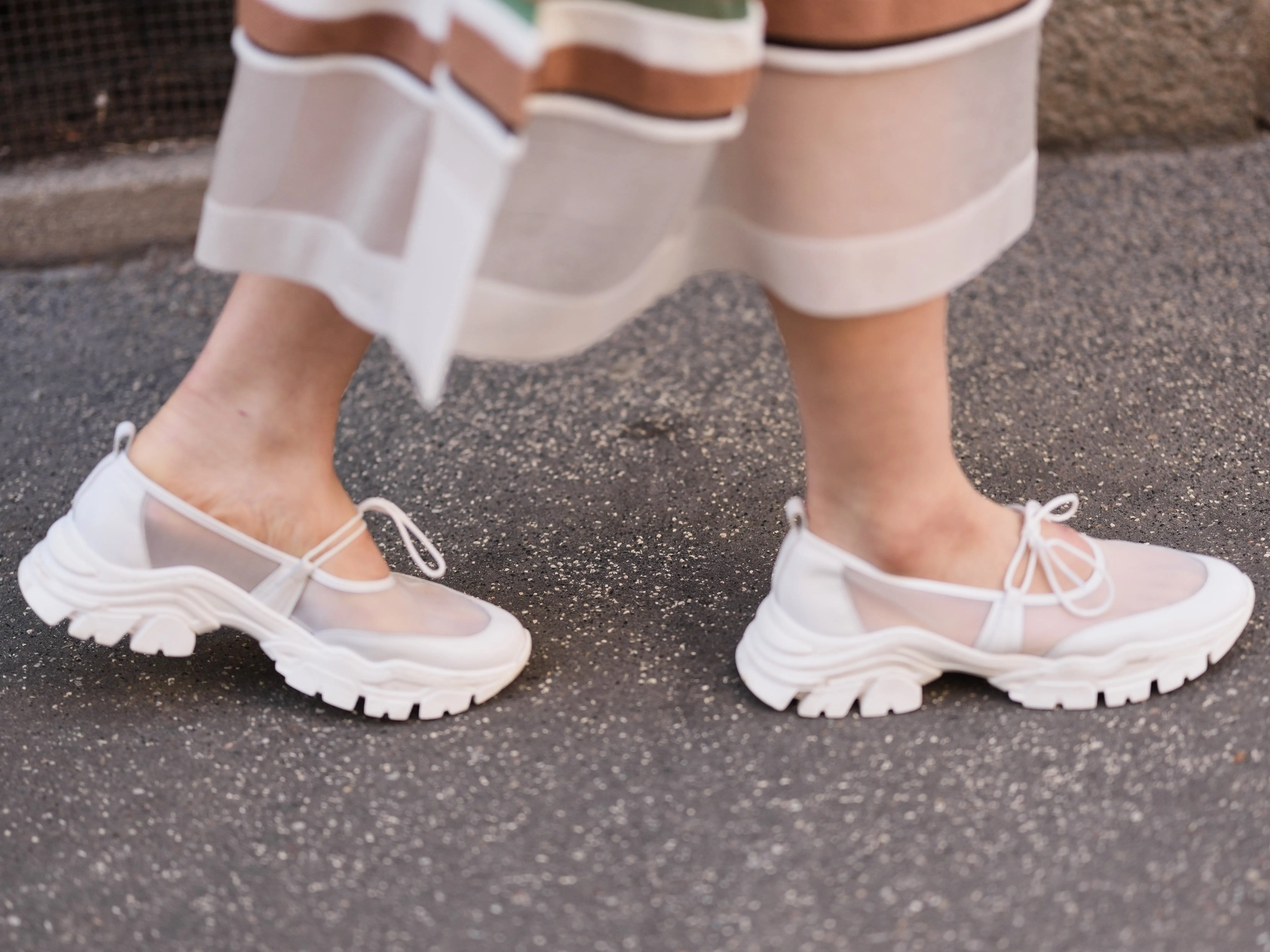 A woman wearing a pair of low-profile white sneakers with mesh details and small strappy laces.