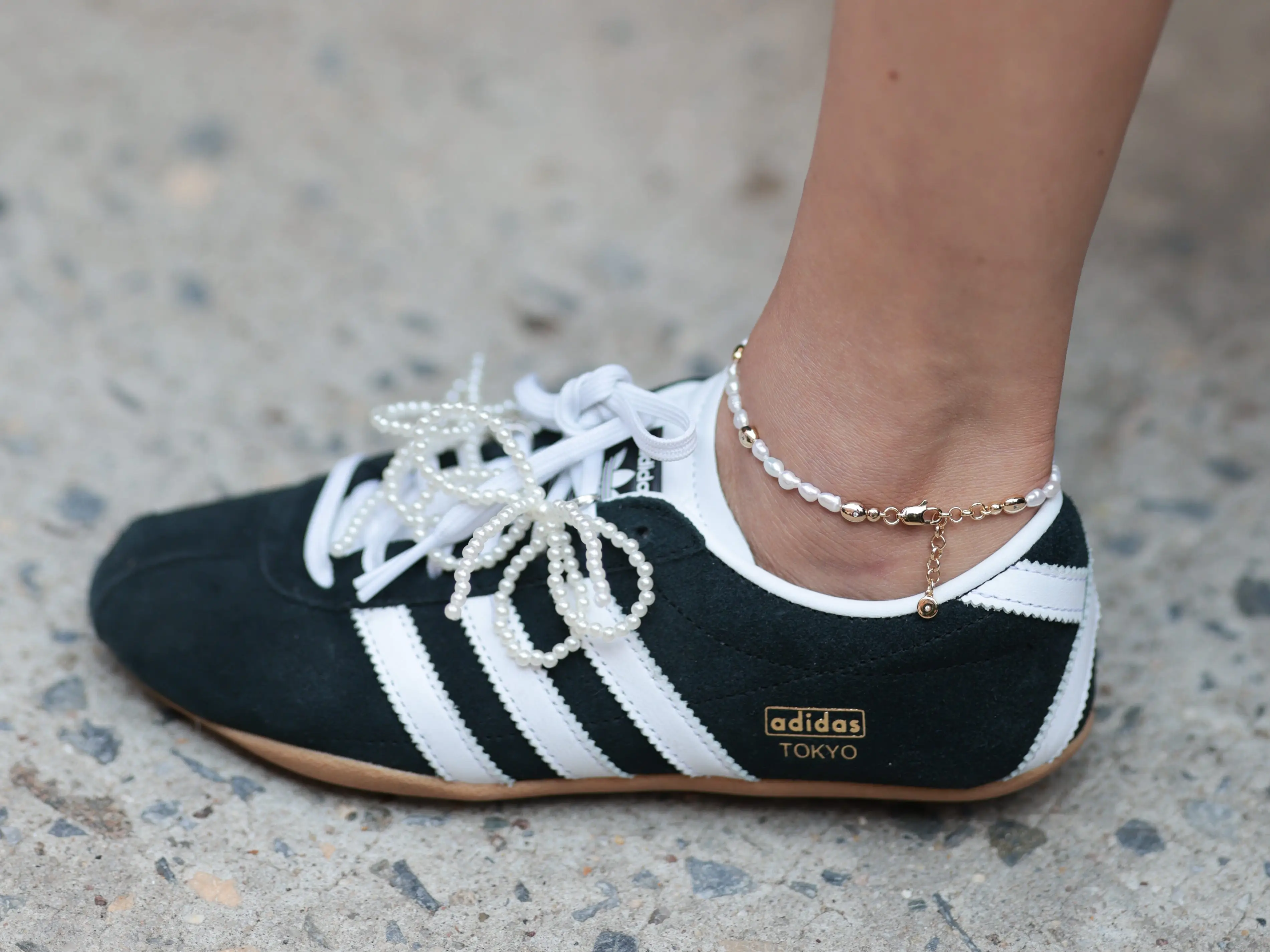 A woman wearing low-profile black-and-white Adidas Tokyo sneakers.