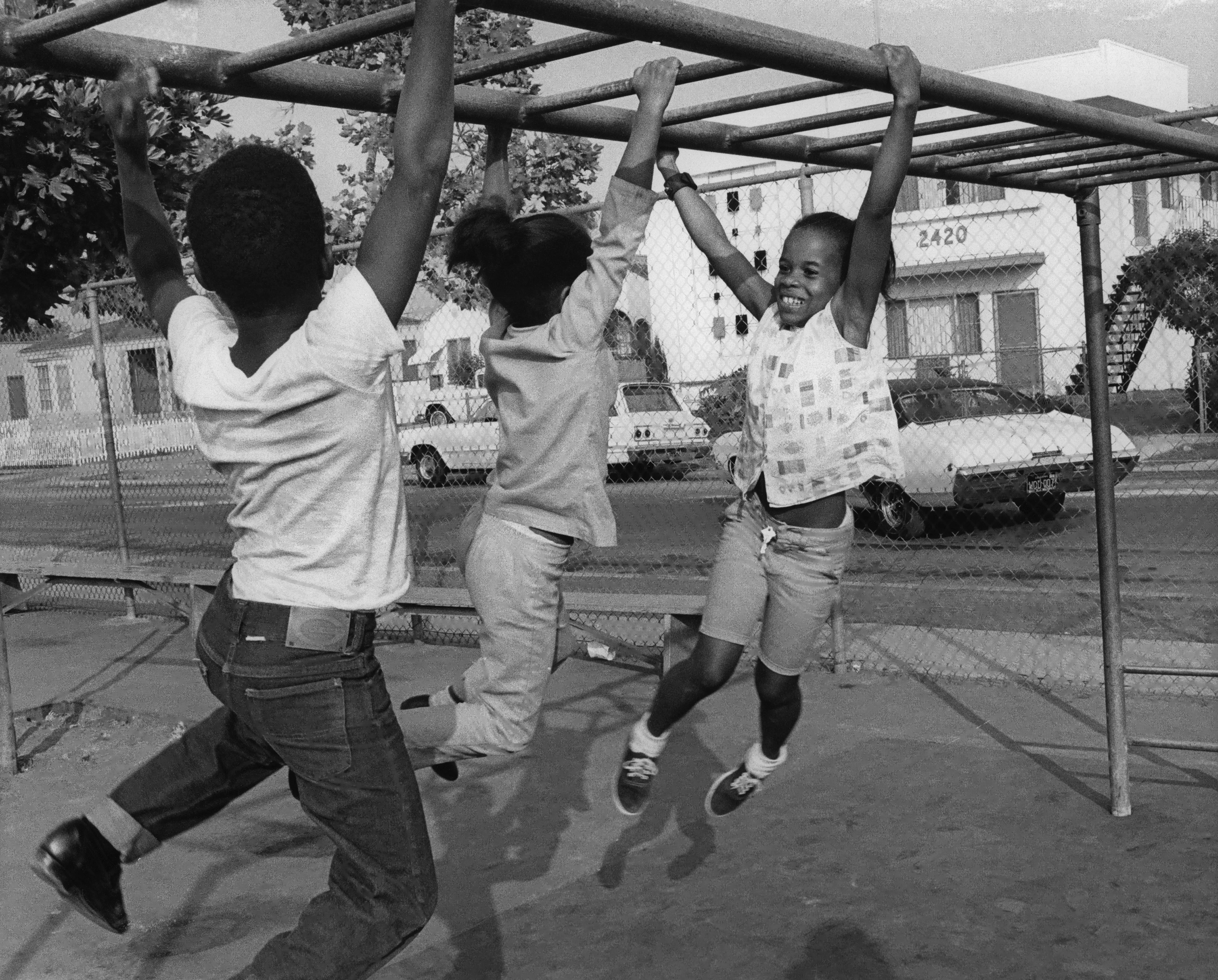 Three kids play on monkey bars at a playground.