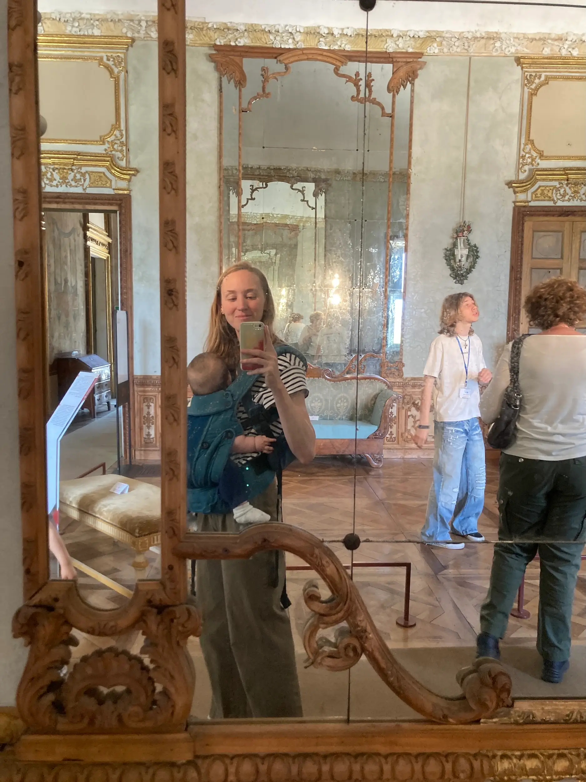 A woman taking a photo in a mirror with a baby strapped to her.