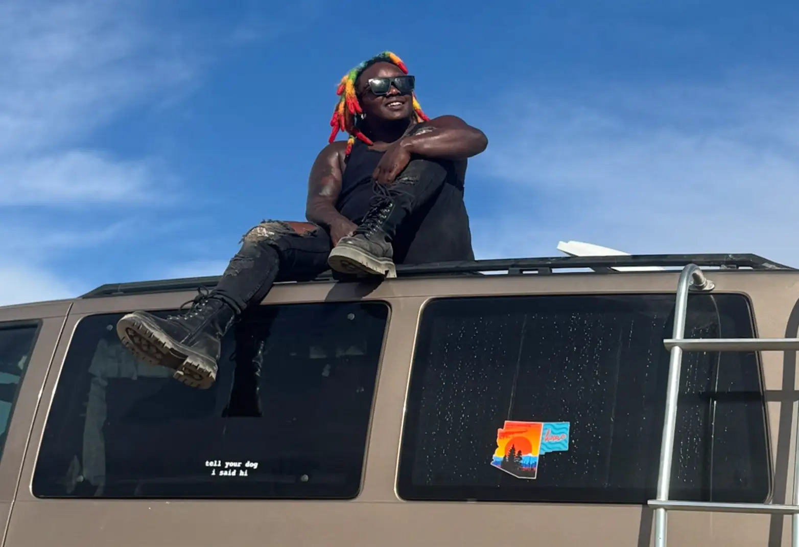 The writer sitting on the roof of their van, with a blue sky in the background.