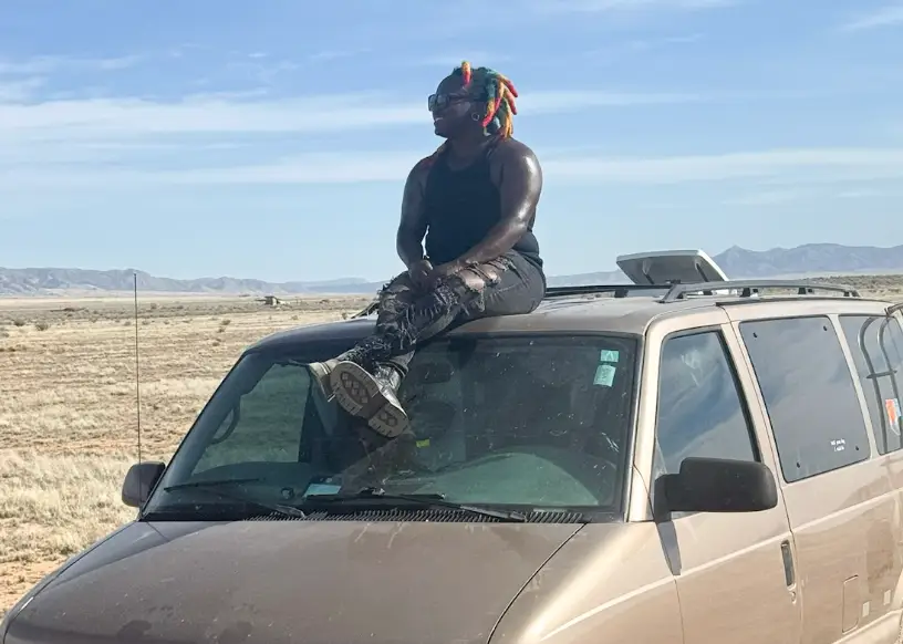 The writer sitting on top of a van in a desert.