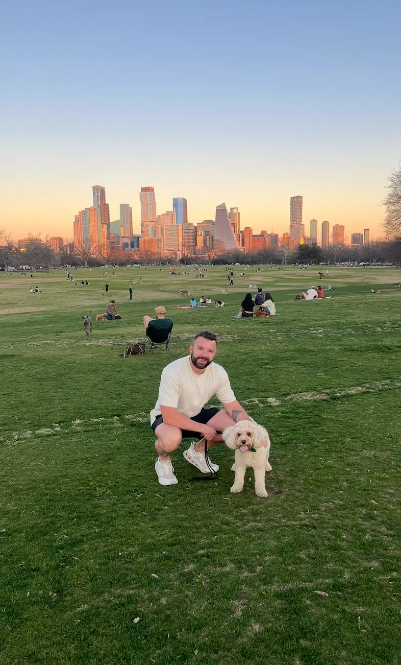 A man kneeling in a park with a dog.