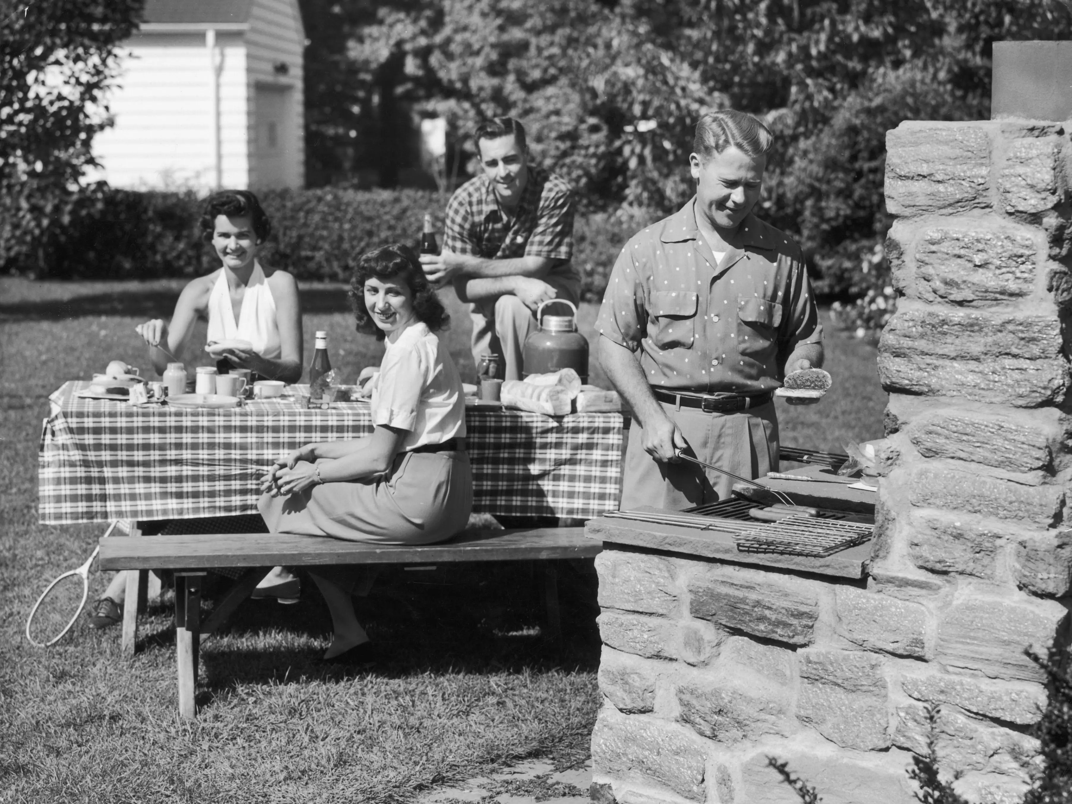 A man grills food outdoors while people sit at a table