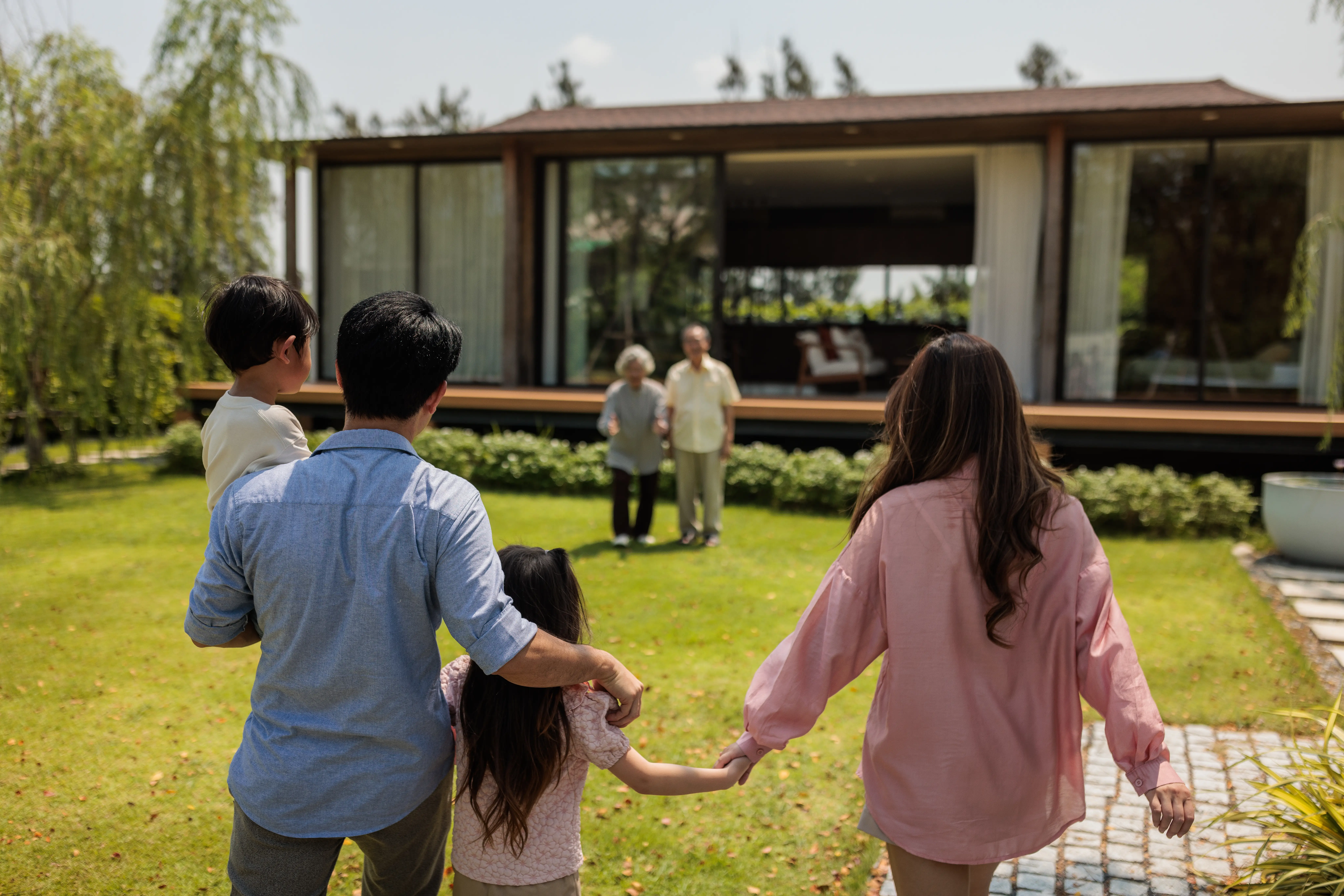A young family walks towards an older couple outside of a home.