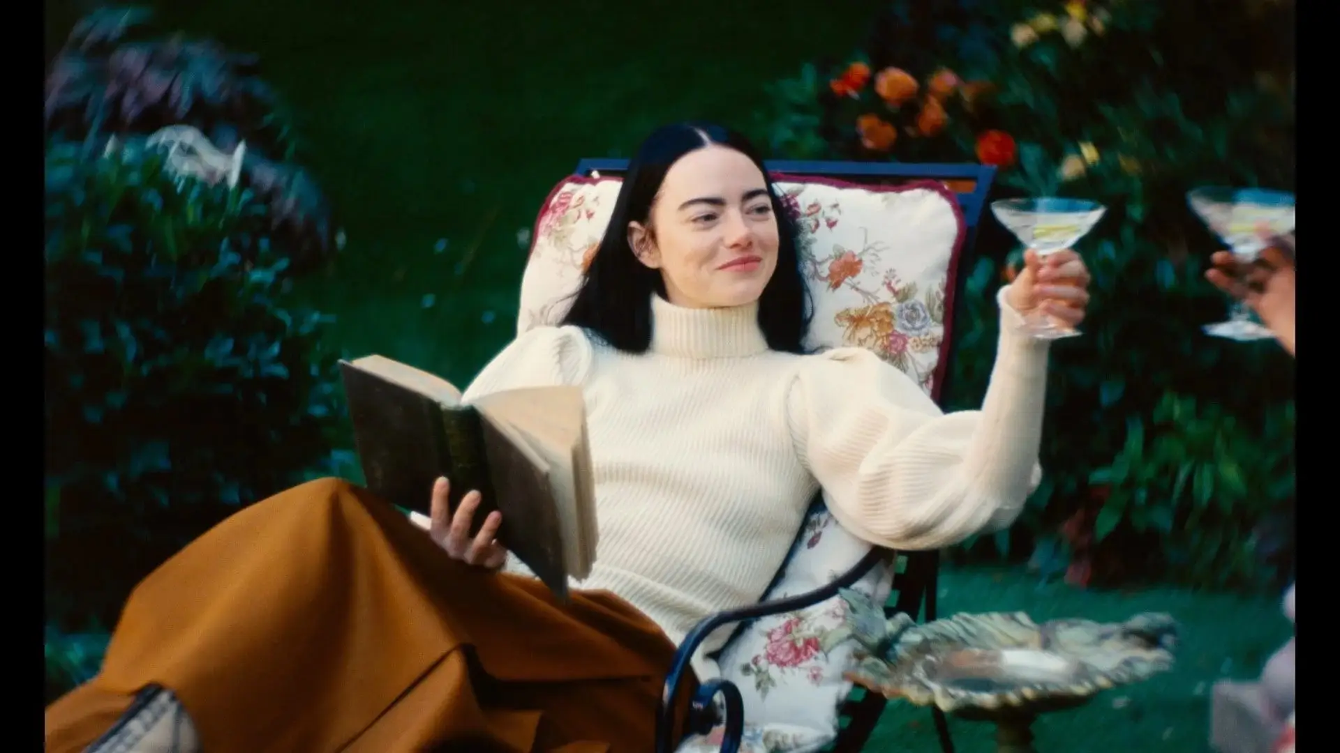 Emma Stone raising a glass while sitting on a chair