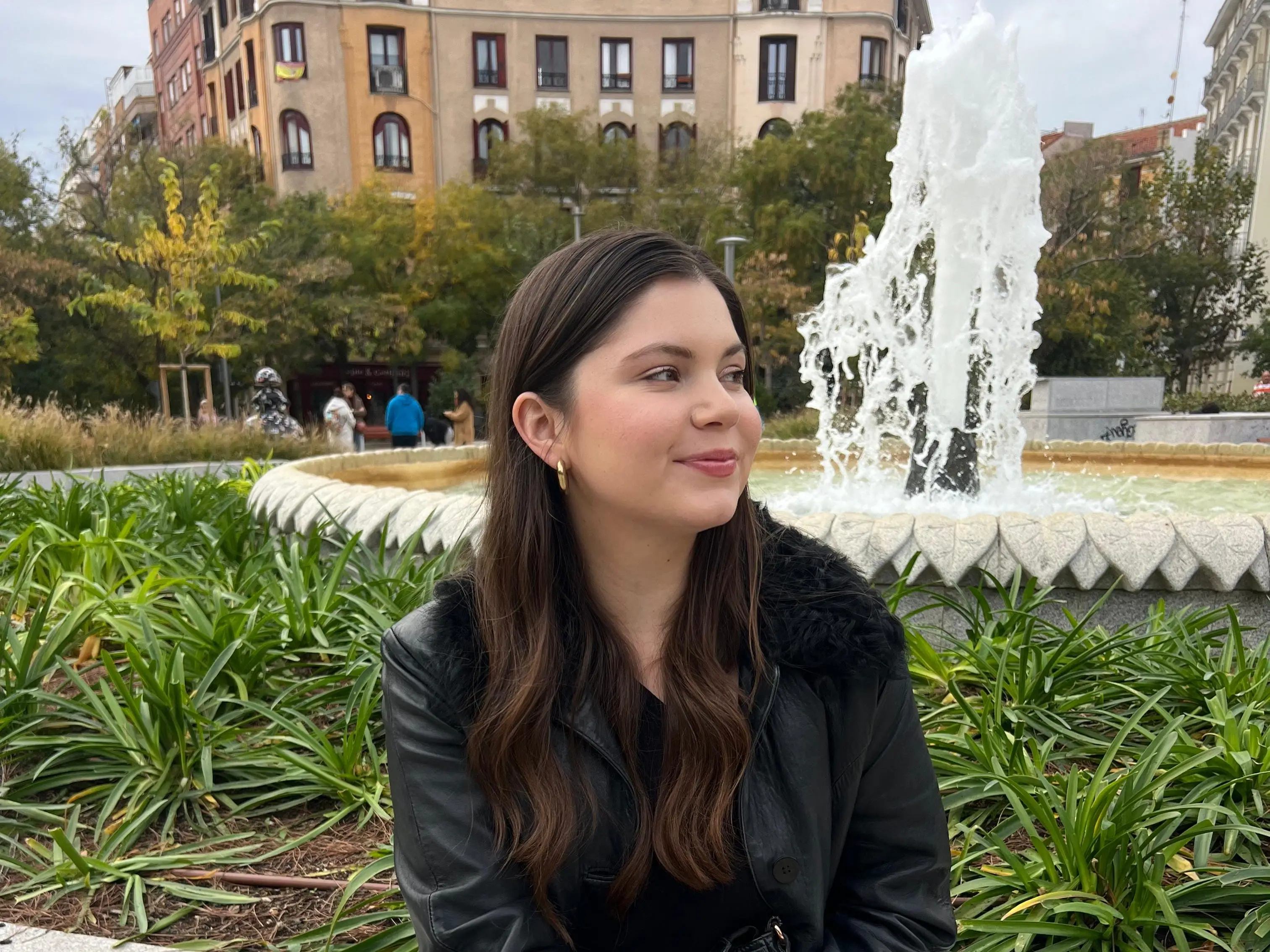 The writer wearing a black jacket and sitting in front of a fountain in New York.