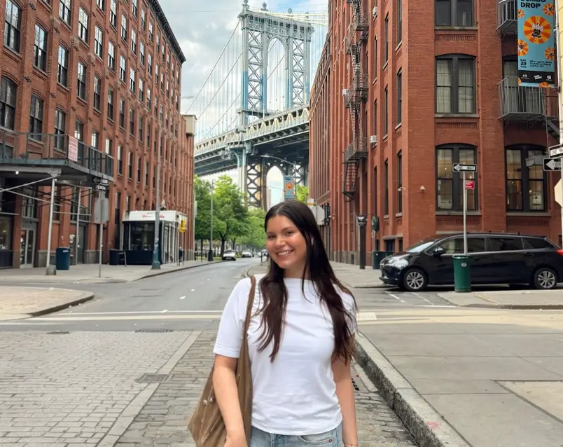 The writer wearing a white tee and standing in front of a bridge in Brooklyn.