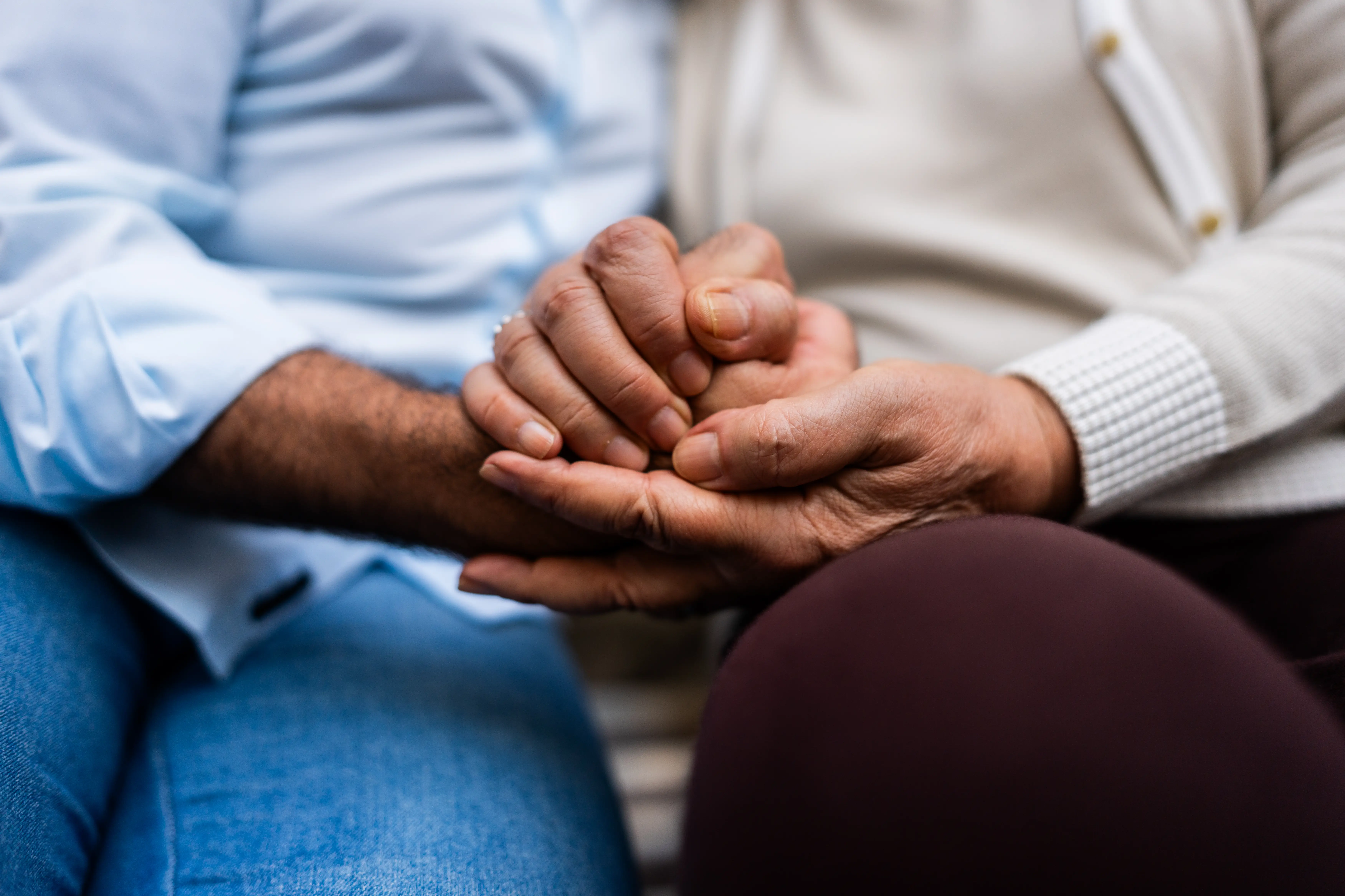 A son and elderly mother hold hands.