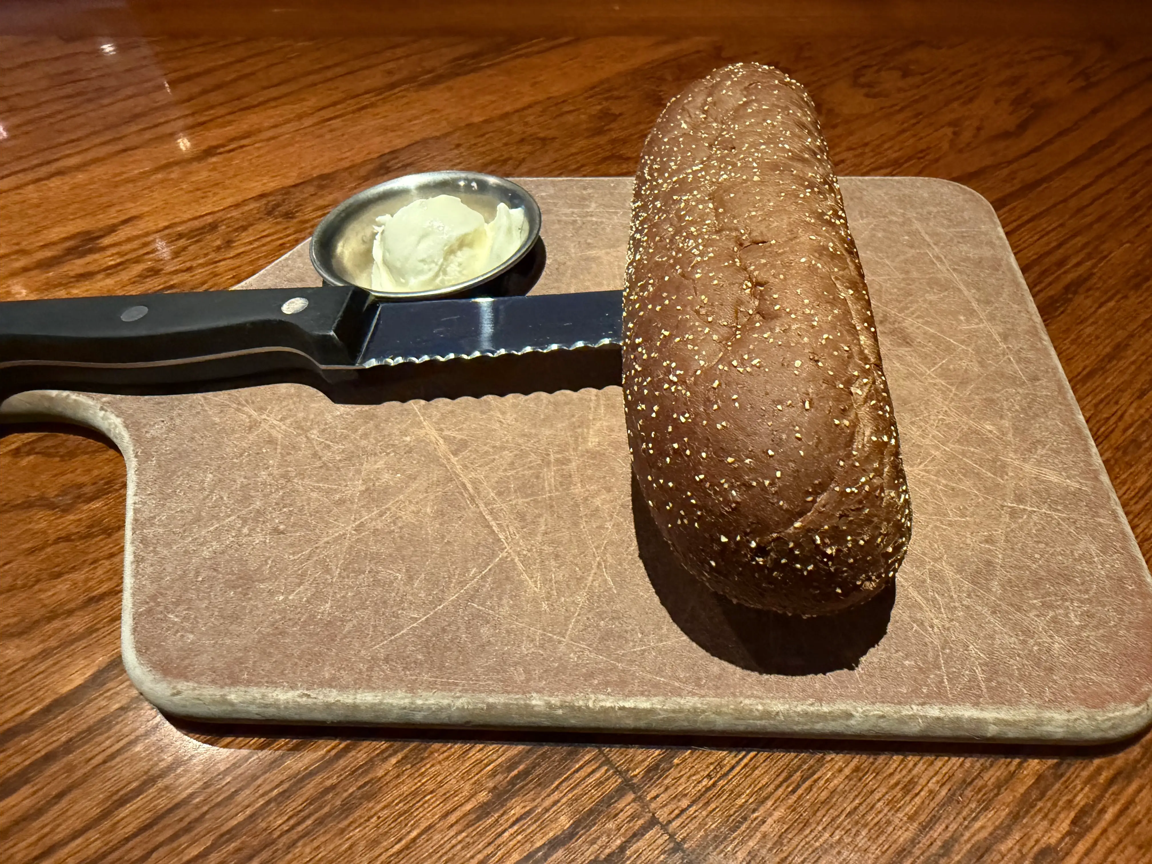 Outback brown bread skewered with knife on cutting board with side of butter