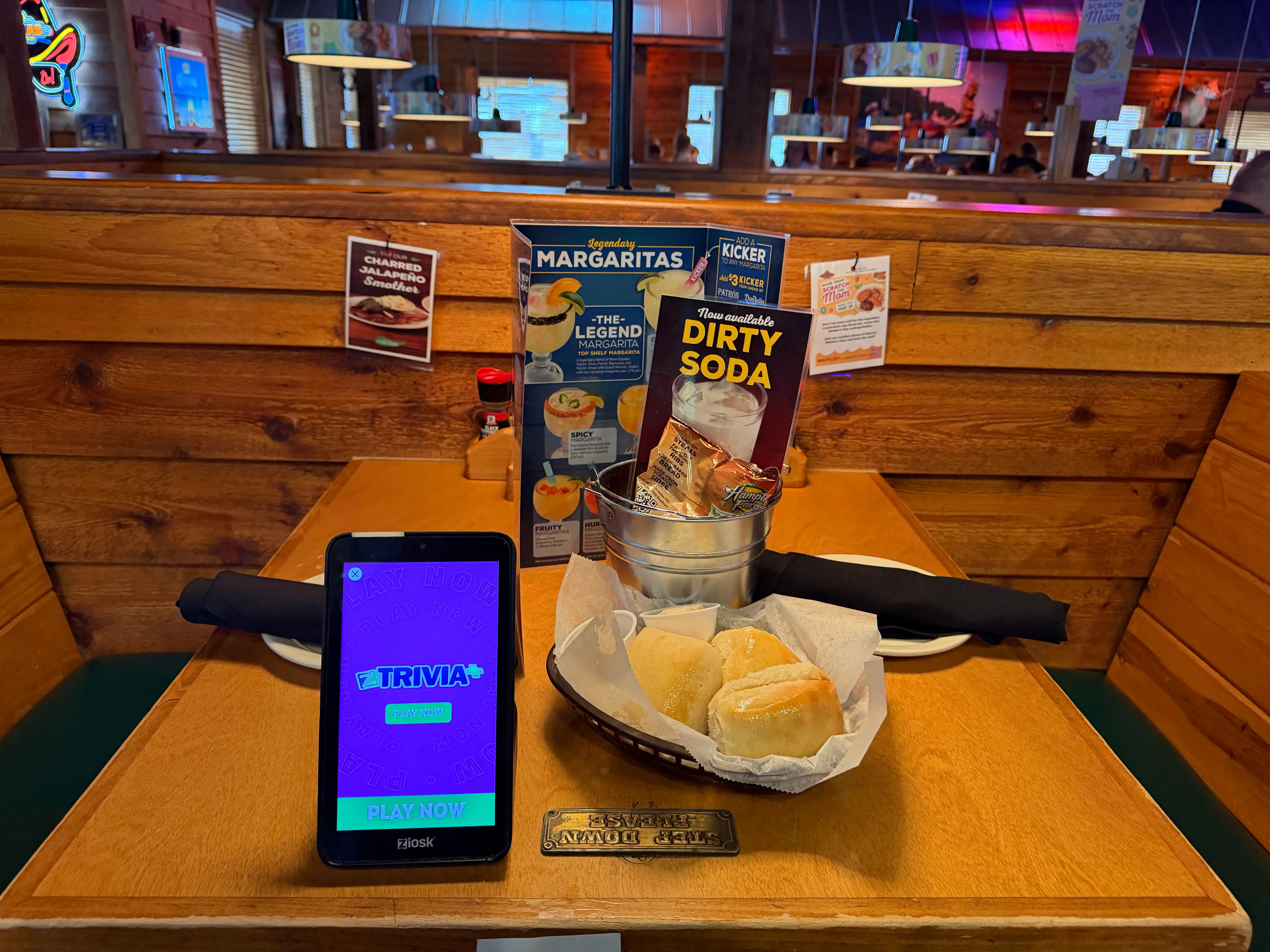 Table at Texas Roadhouse with basket of rolls, cutlery, plates, peanuts in metal bucket
