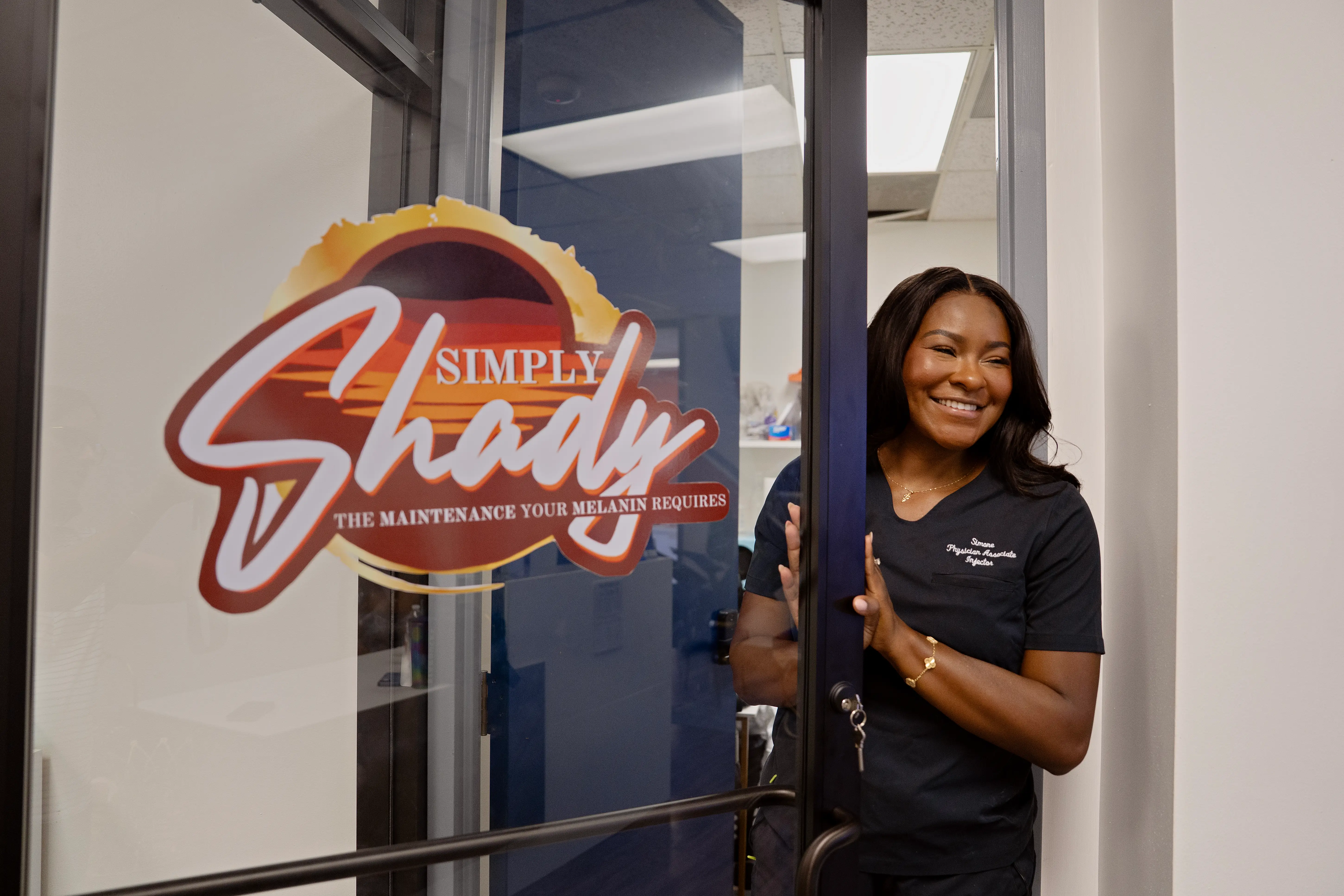 Simone, founder of Queen Aesthetics, in front of a spa door with Simply Shady branding on it.