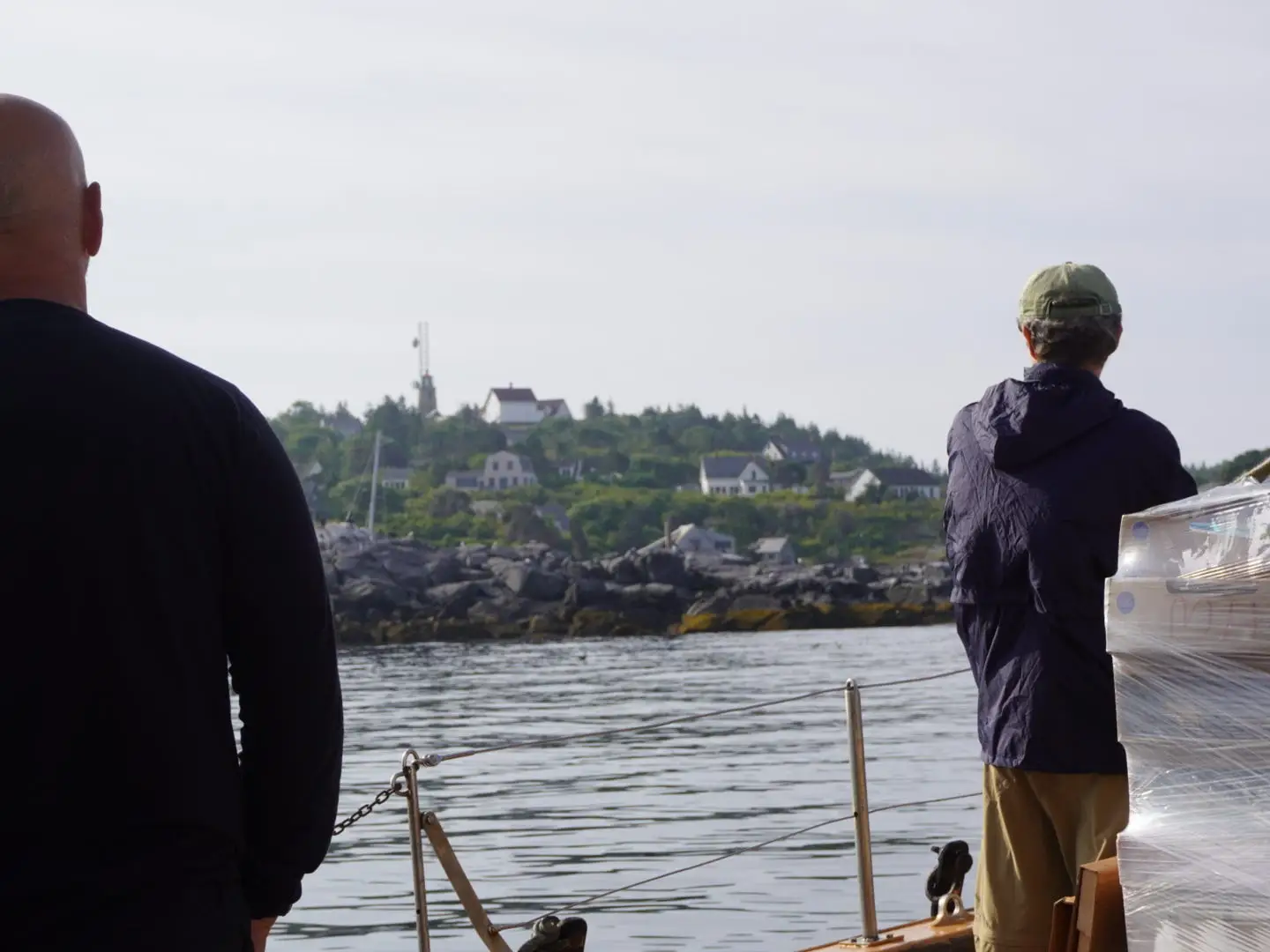 Two men stand on the deck of a ship that's pulling into Monhegan Island.