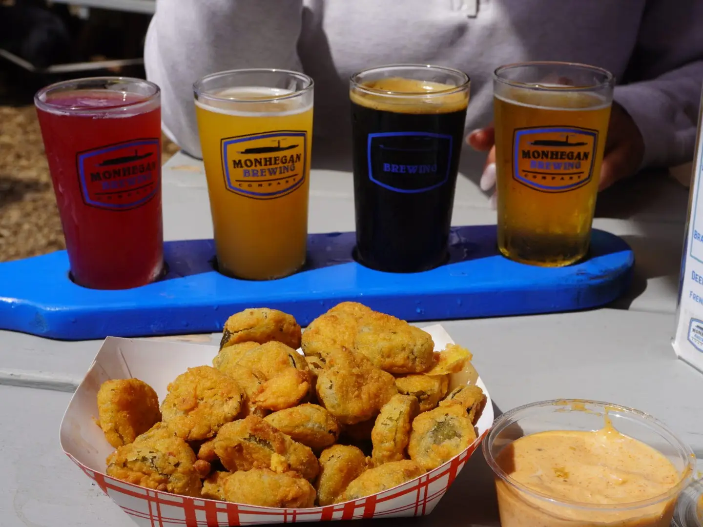 A flight of four beers and an order of fried pickles on a table.