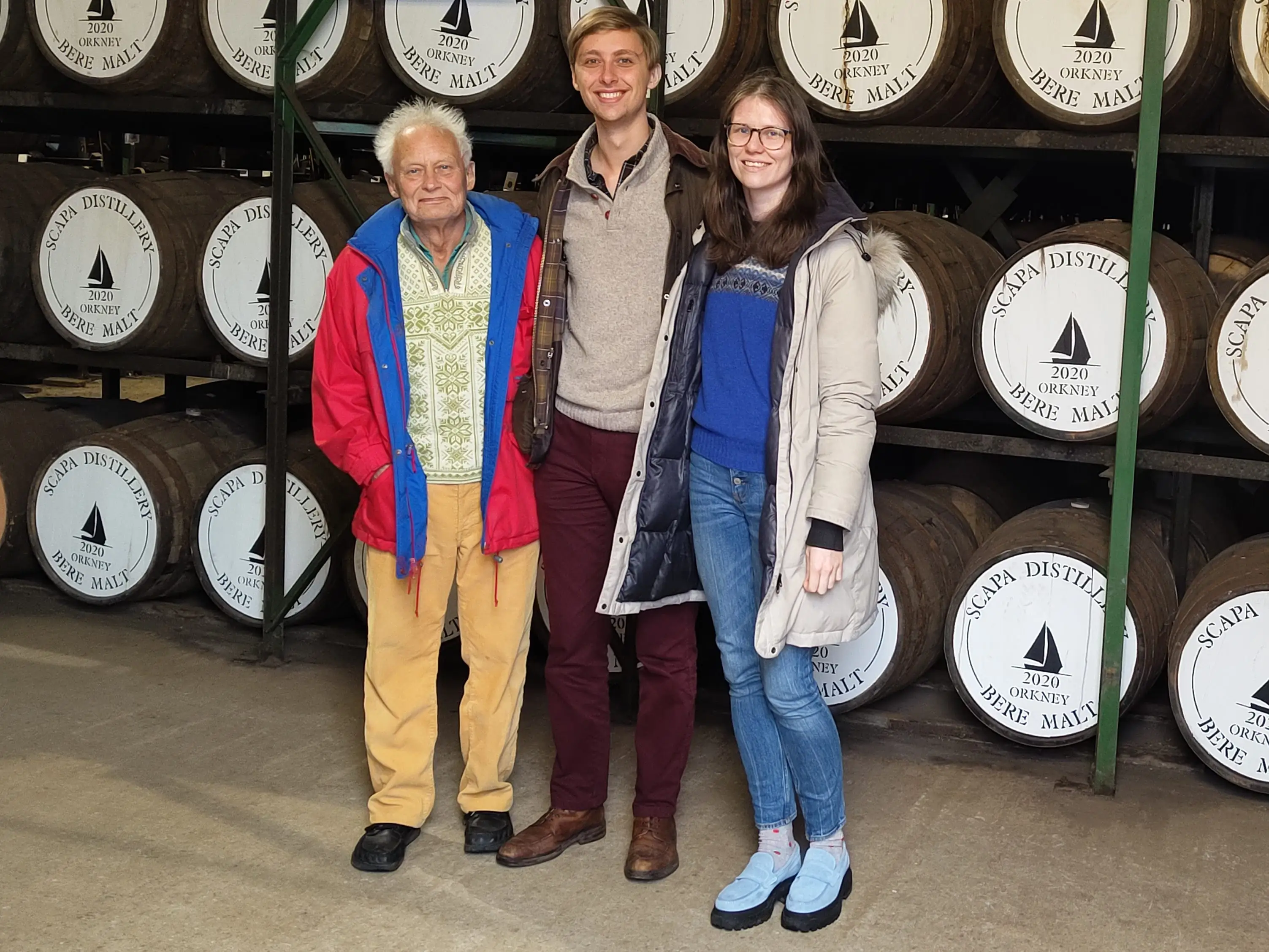 Heather, her husband, and her father-in-law pose for a photo in a distillery.