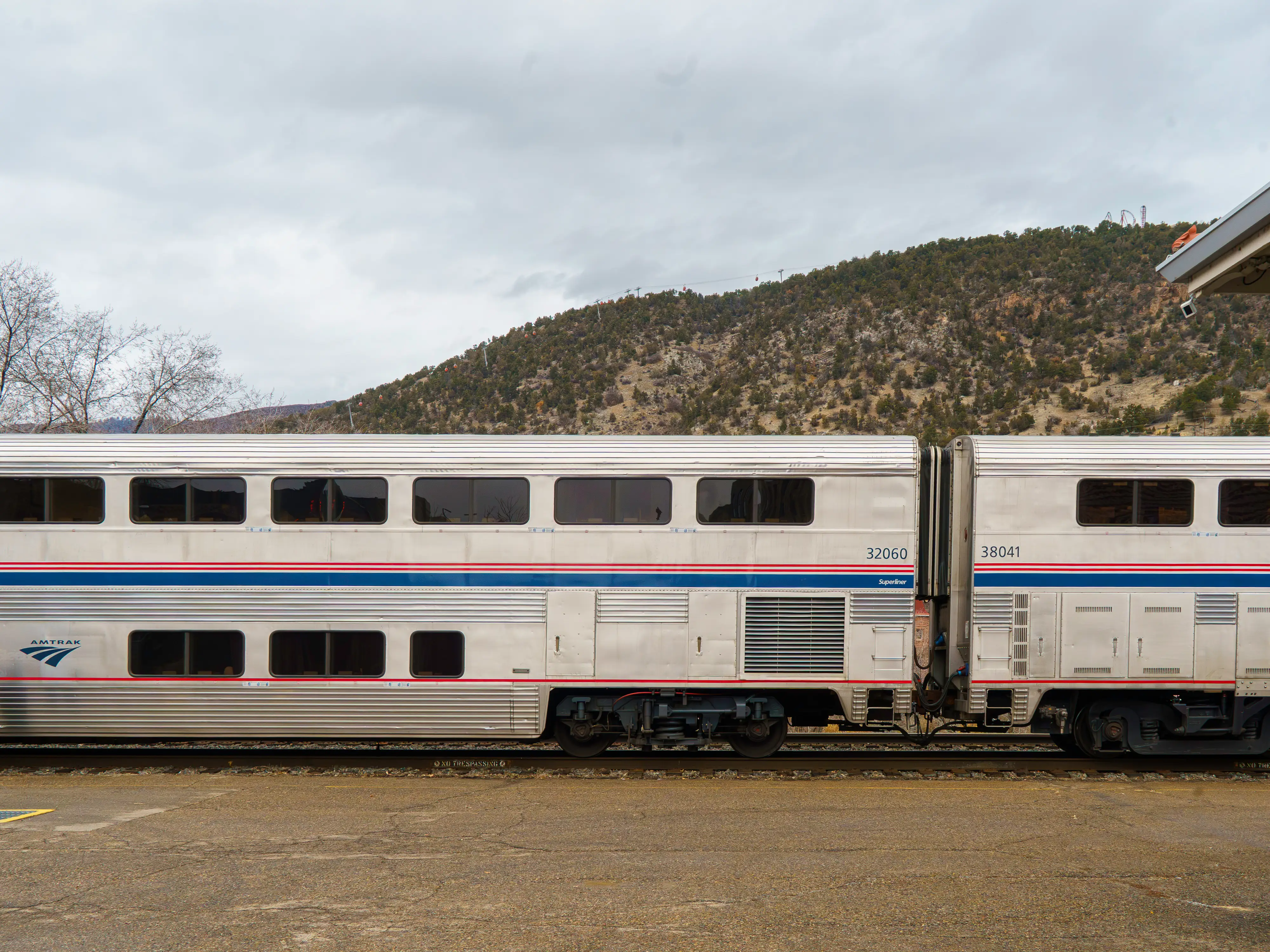 An Amtrak California Zephyr train stopped in front of a hill on a cloudy day