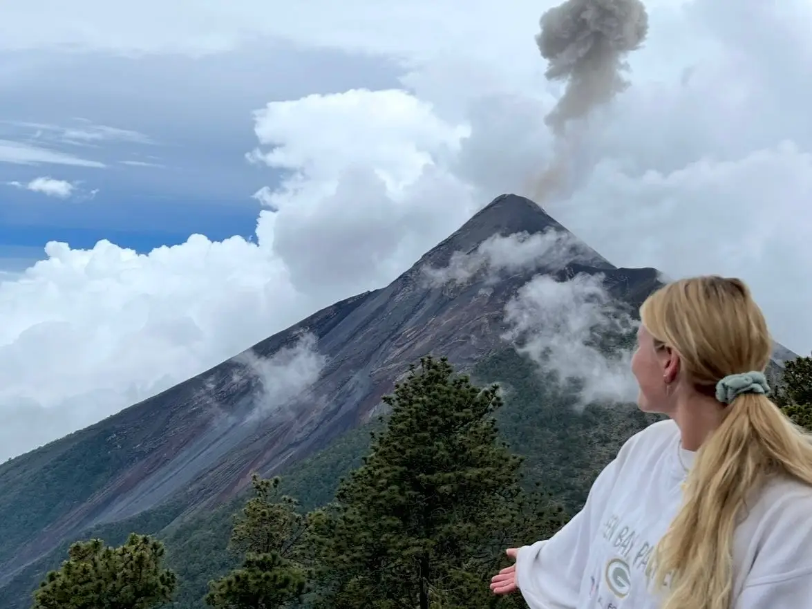 A woman standing in front of Volcán de Fuego, an active volcano, in Guatemala.