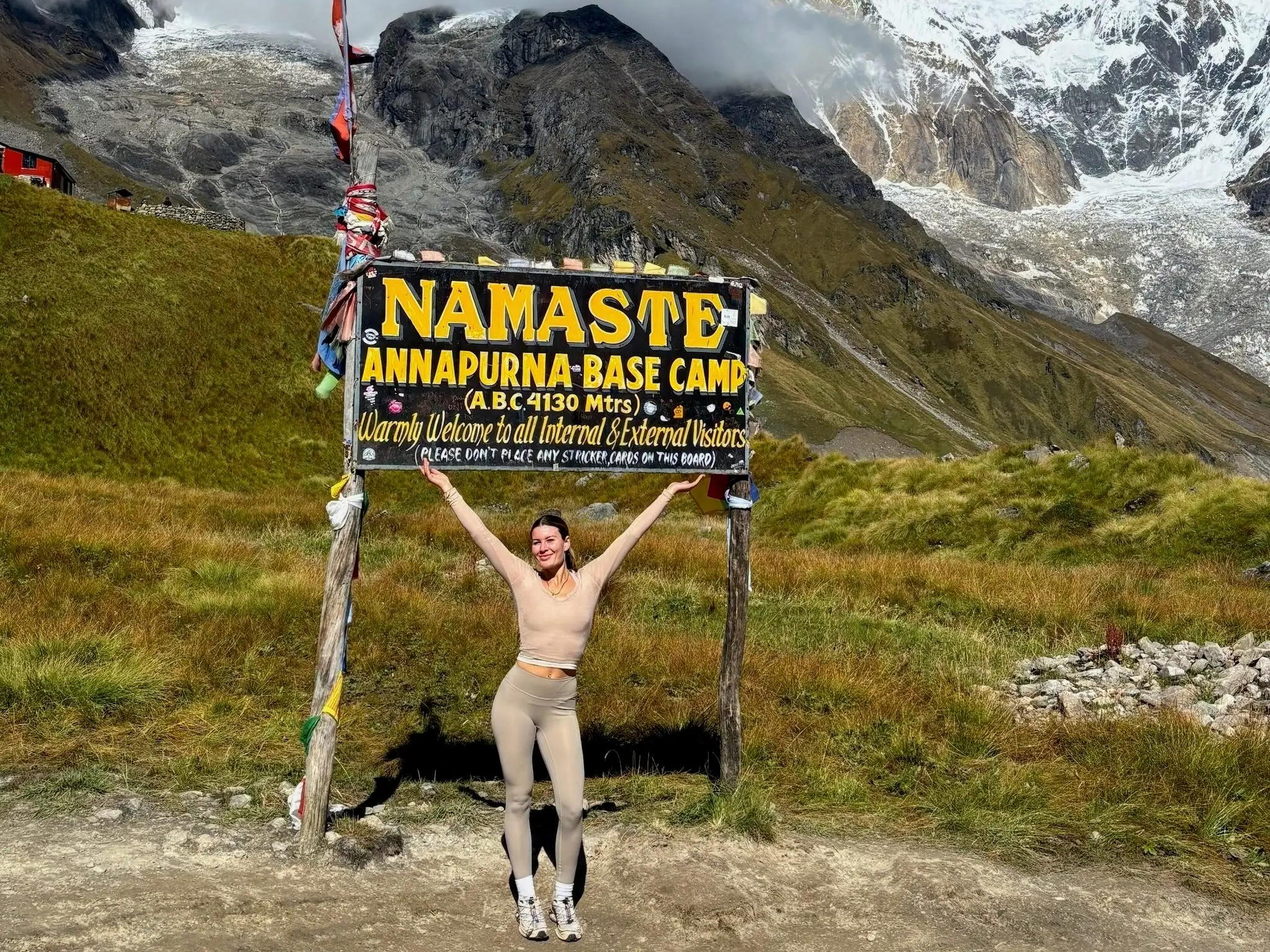 A woman standing in front of a sign for Annapurna Base Camp in Nepal.