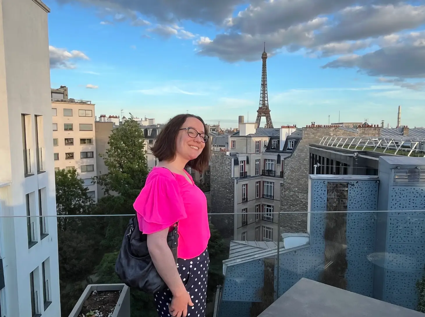 The writer wearing a pink top and standing on a Paris hotel rooftop, with the Eiffel Tower in the background.