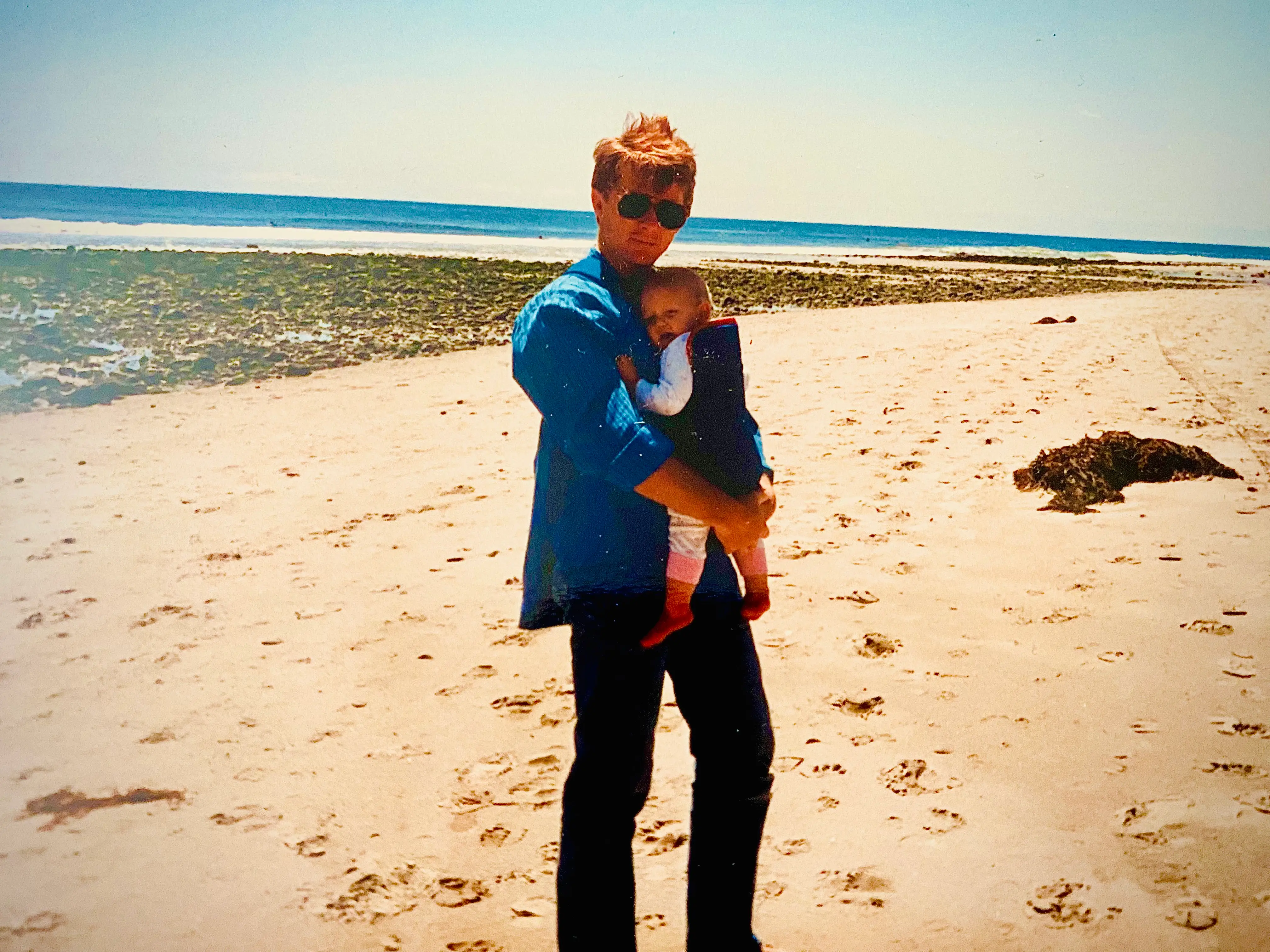Man in sunglasses on beach in Malibu holding baby in carrier
