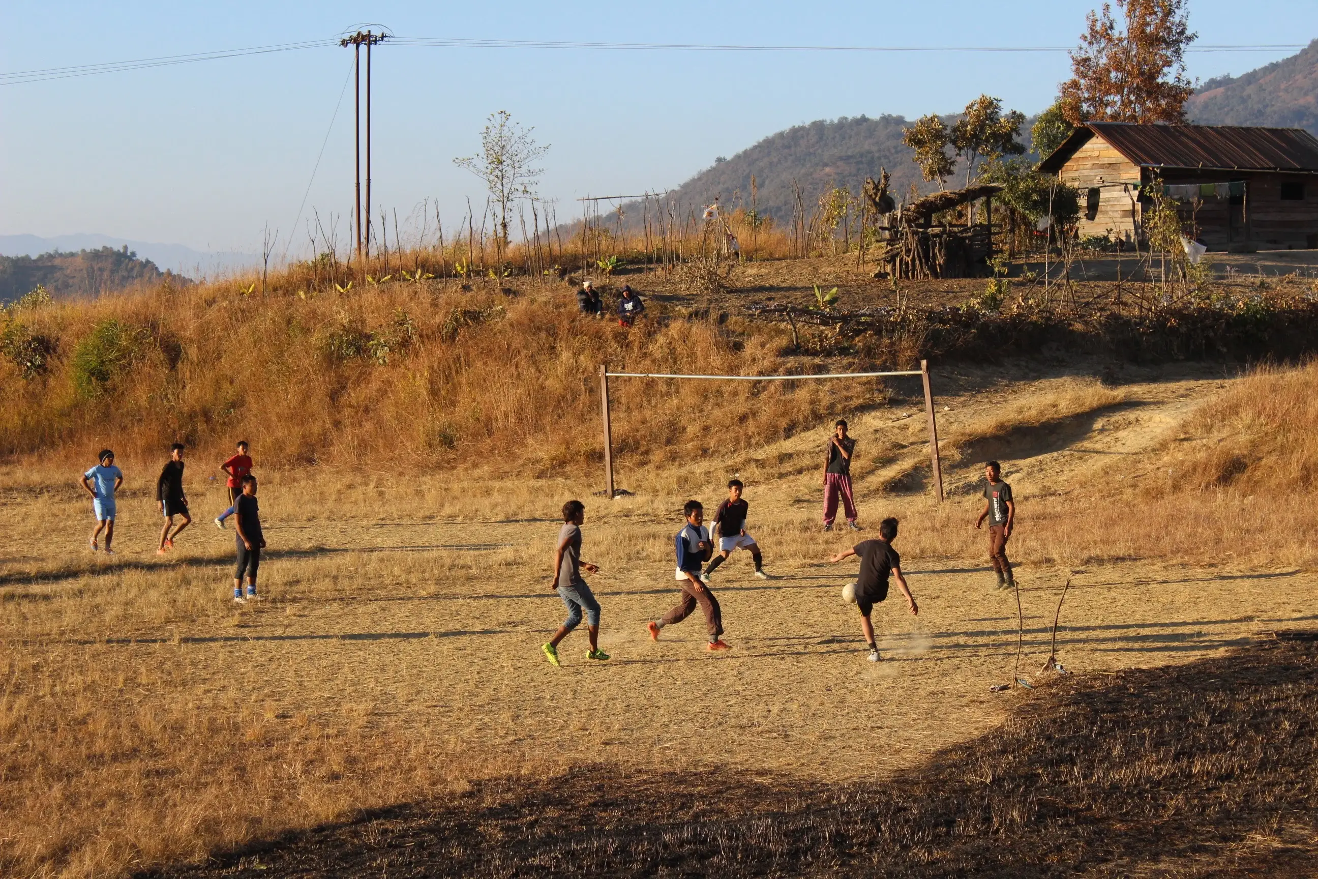 Kids playing soccer on dirt ground.