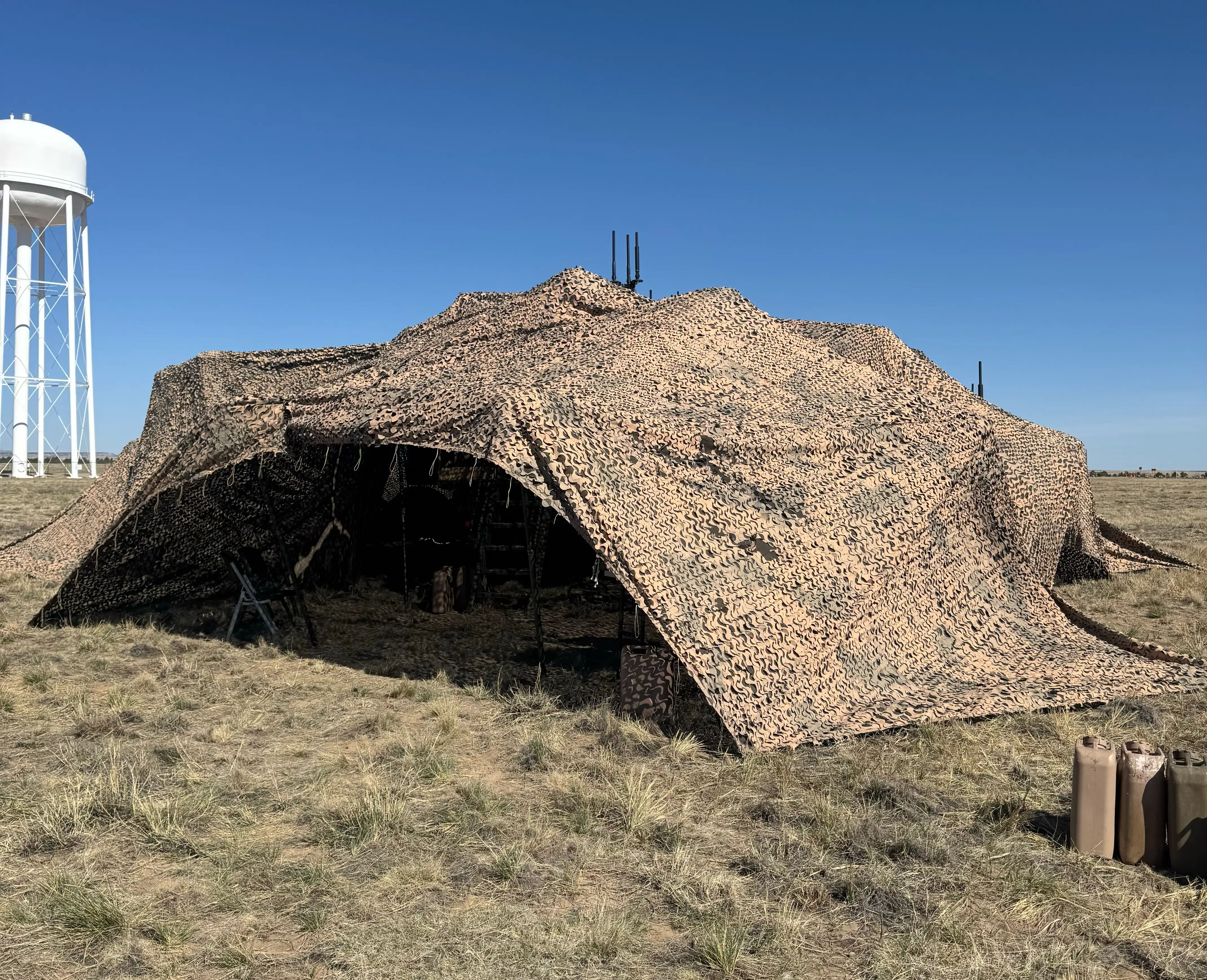 A large camouflage tent sits on brown and green grass.