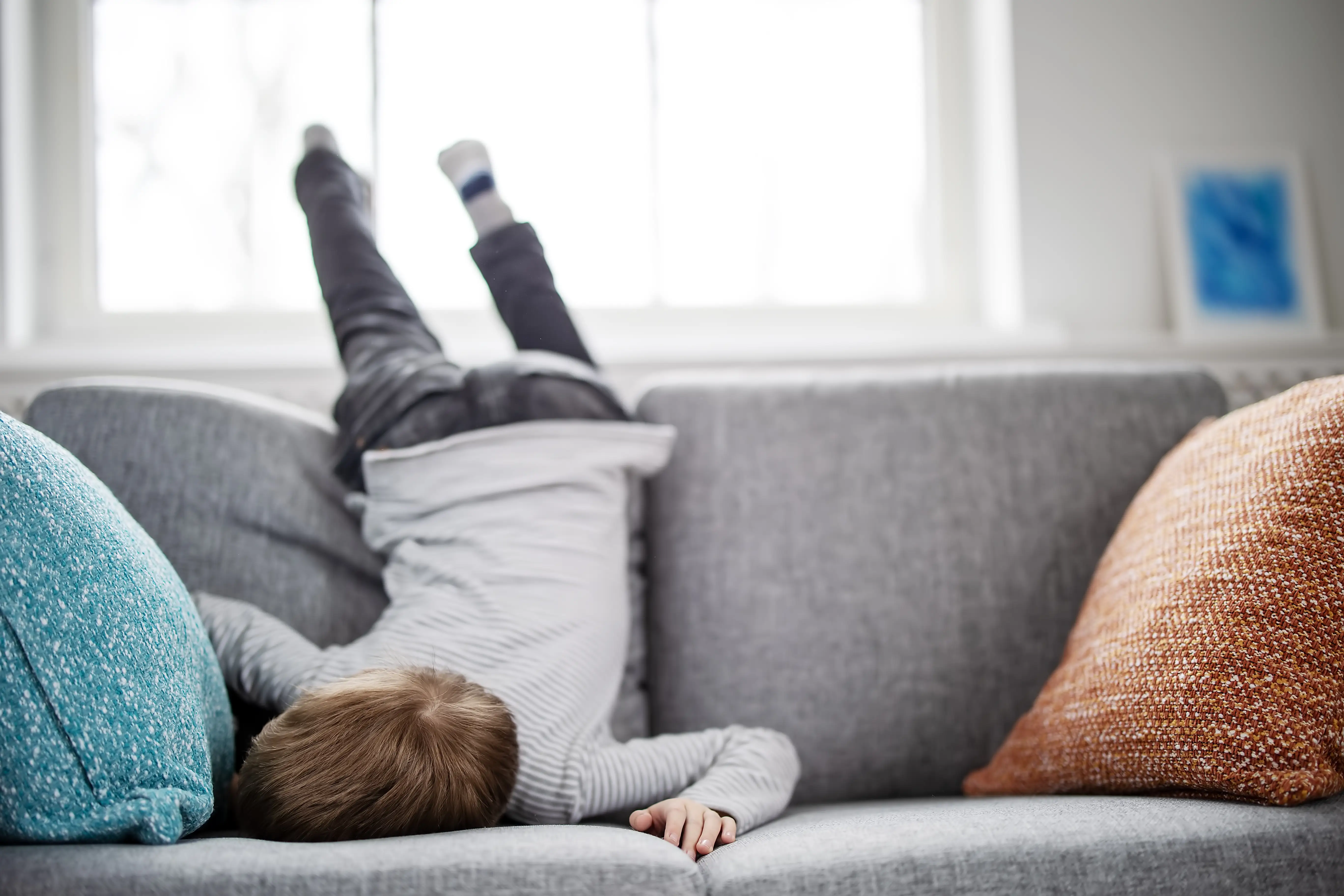 A child flipped over upside-down and backwards on a couch, seemingly bored.