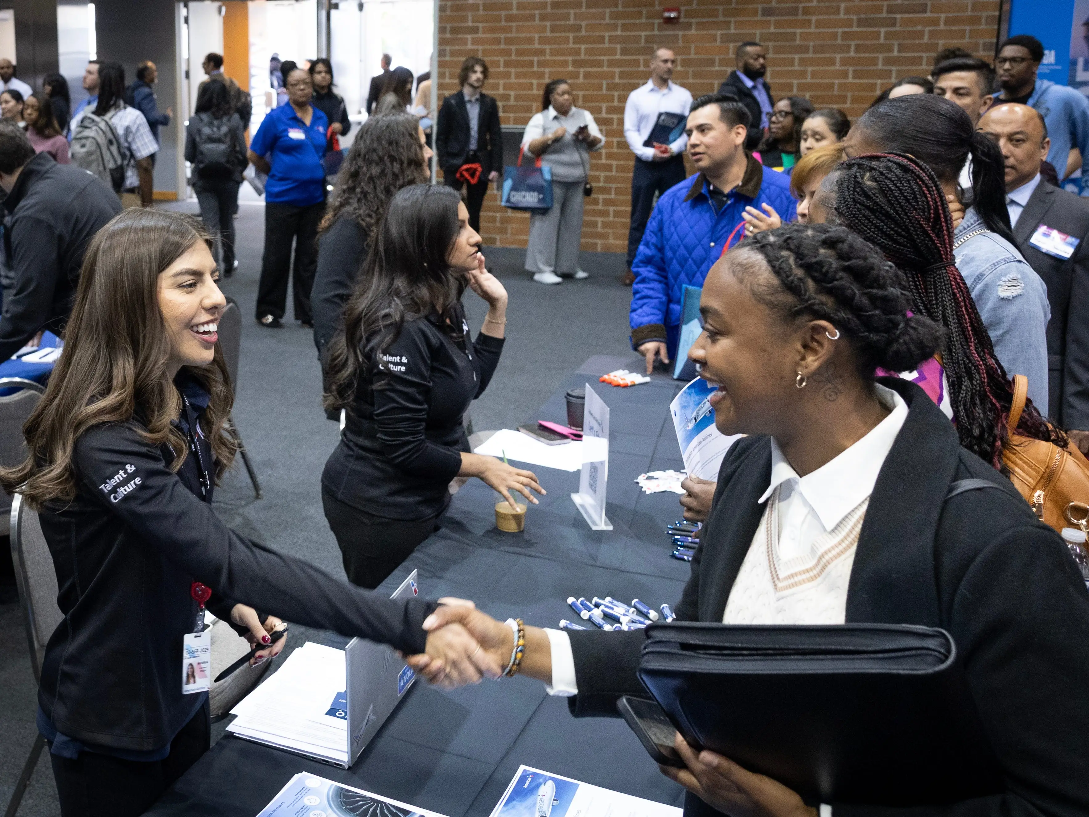 Two people shaking hands and other people around at a job fair