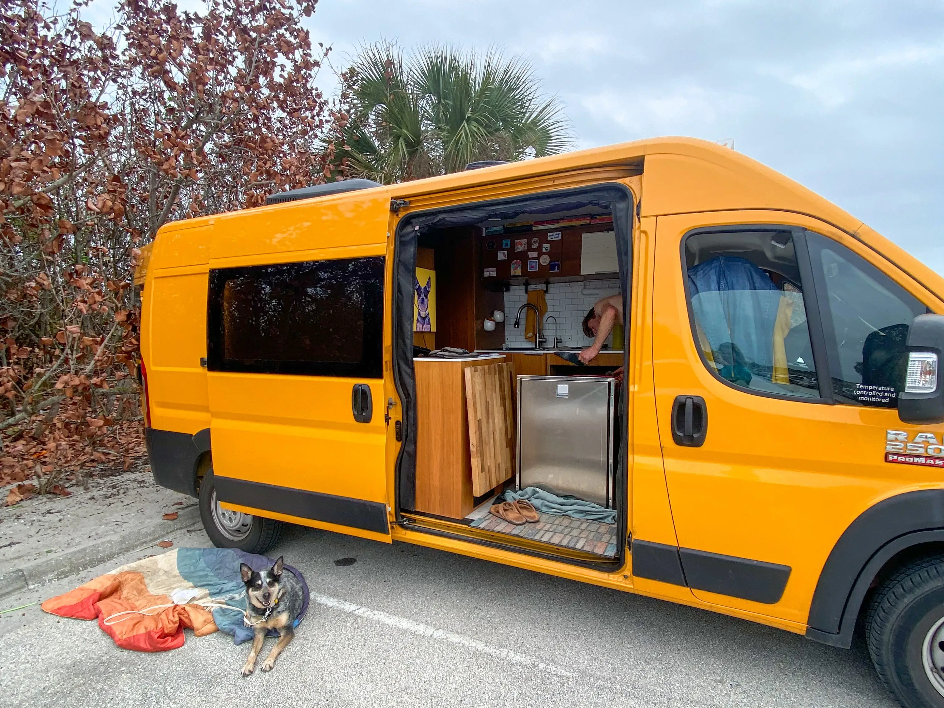 A person doing laundry in a yellow van, with a dog sitting on the ground outside.