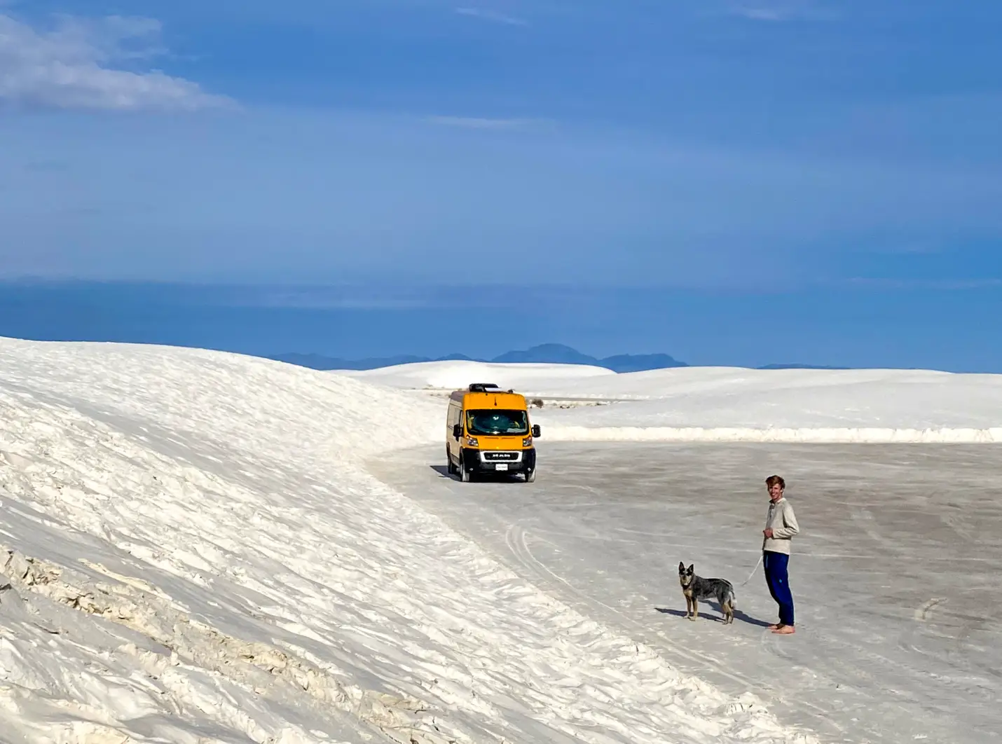 The writer's partner and dog standing near their yellow van in a sandy, sparse environment.