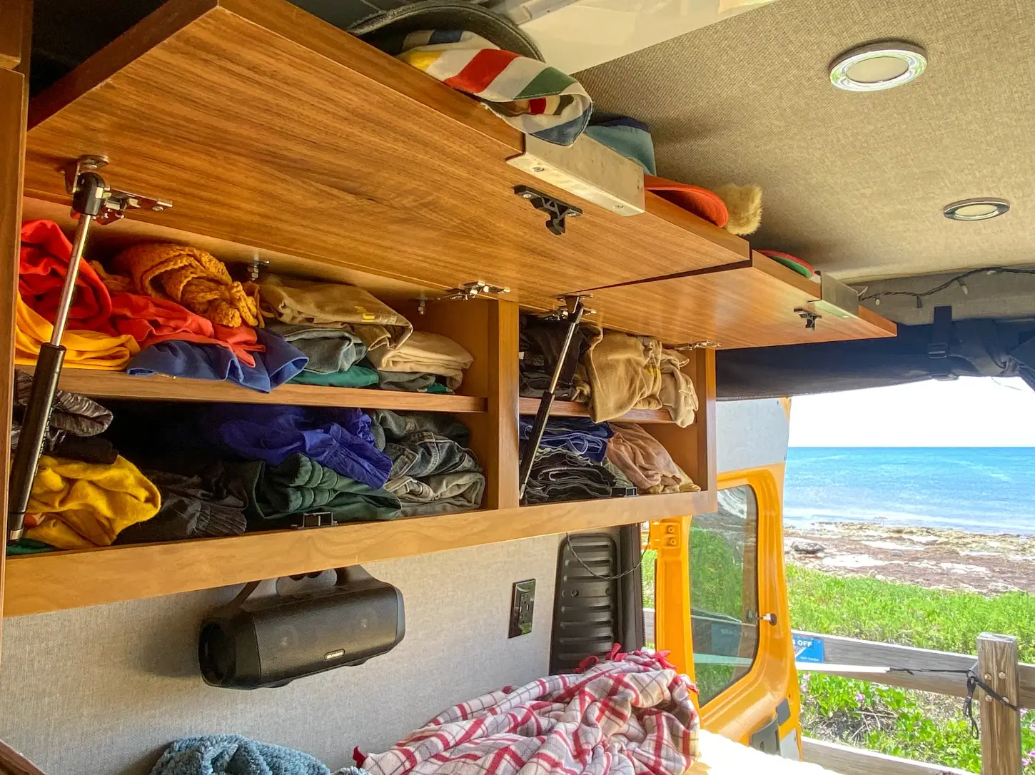 Shelves of closet storage in the writer's van, with the beach and ocean in the background.