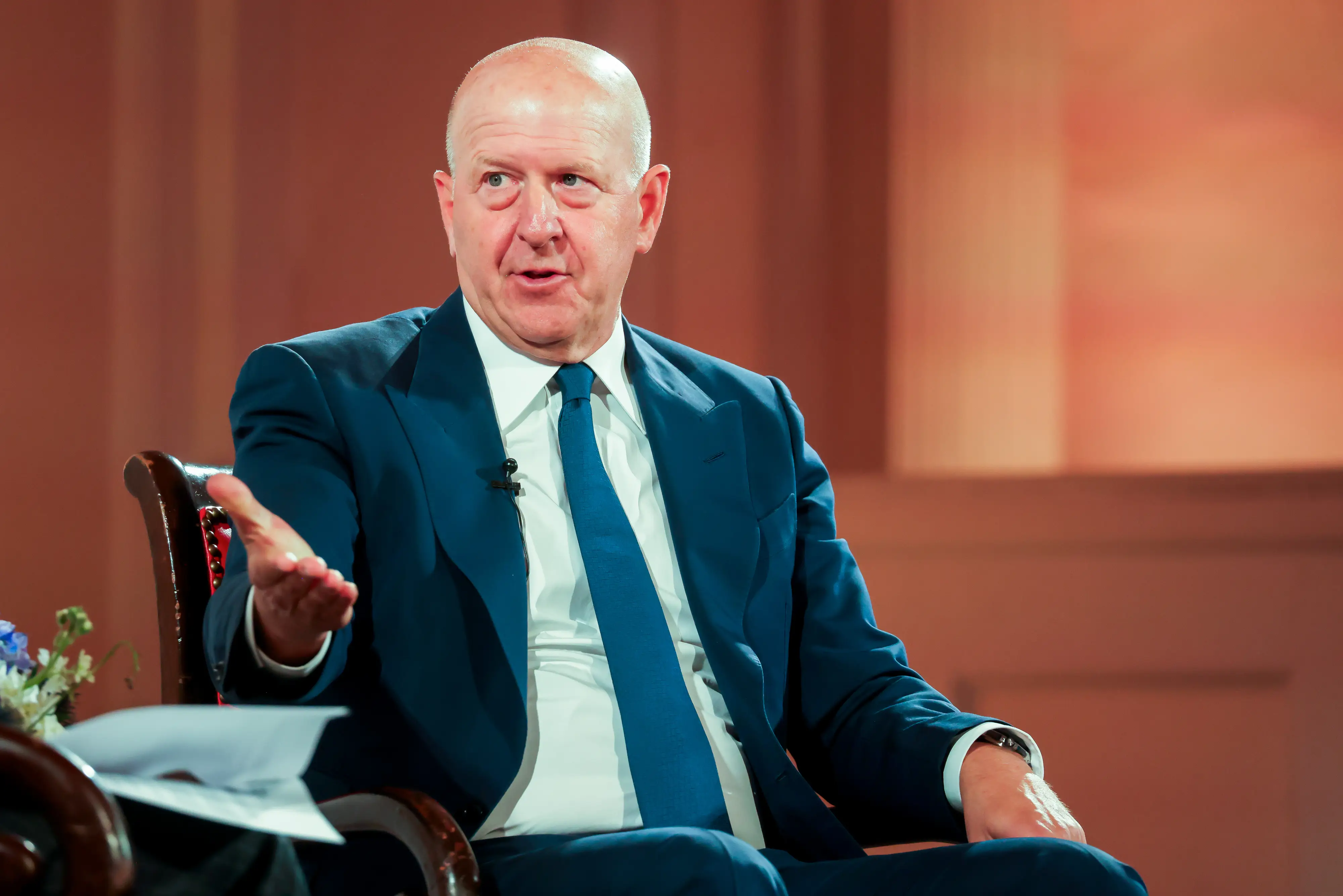 David Solomon gestures with his right hand while sitting in a wooden chair.